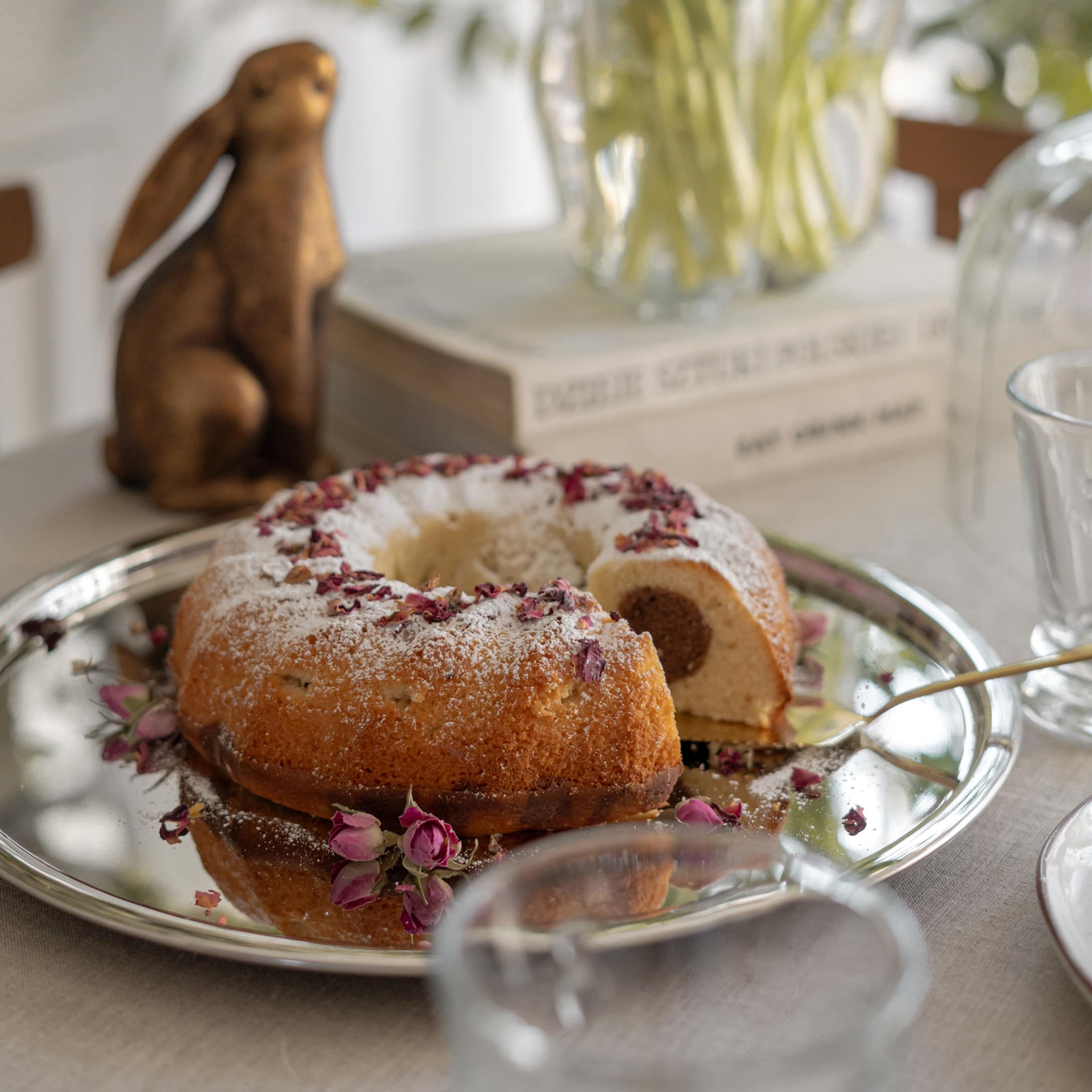 Gâteau en forme de couronne saupoudré de sucre glace et de pétales de rose séchés sur un plateau argenté