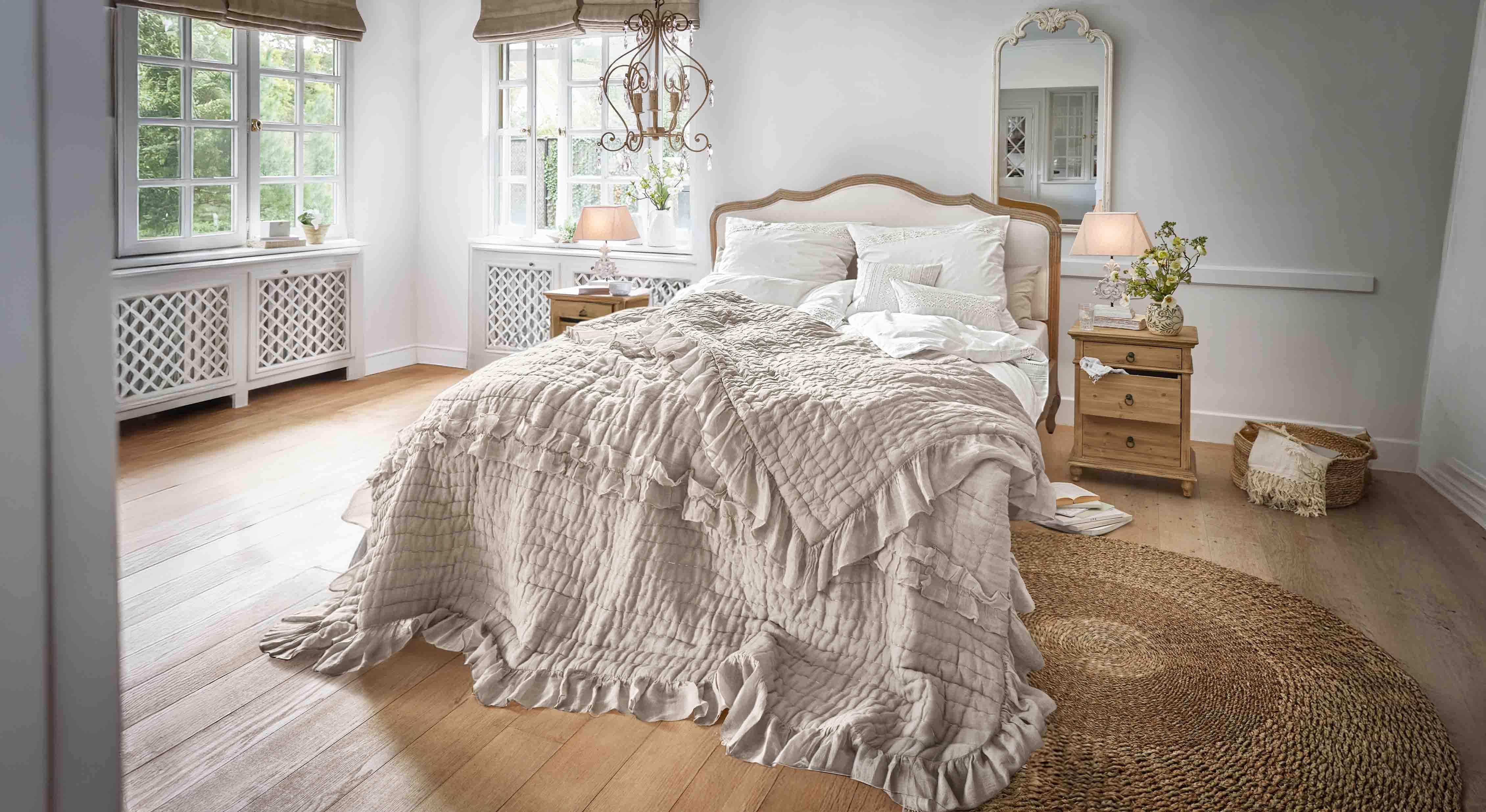 Gezellige slaapkamer met bed in beige sprei met ruches en houten meubels