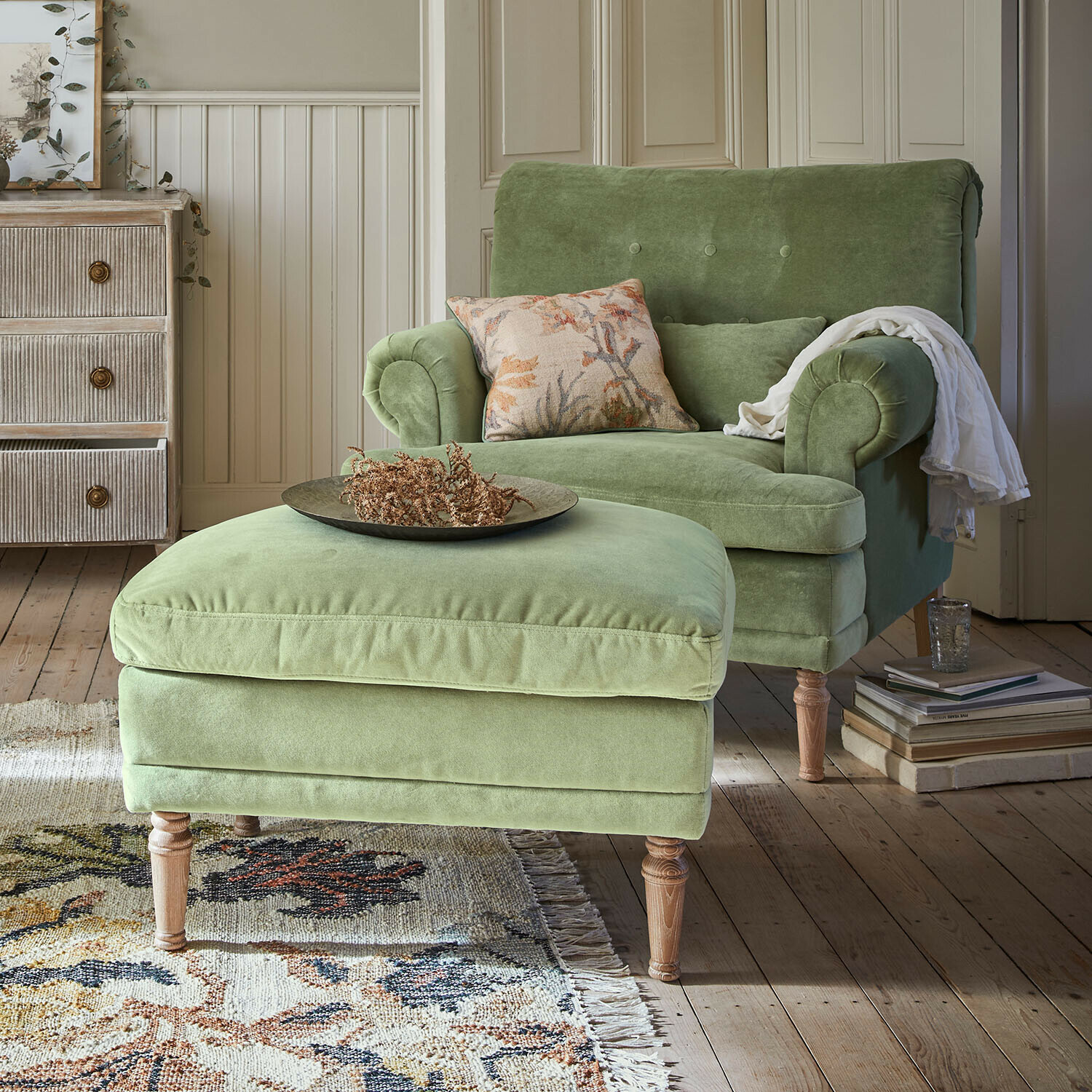 Fauteuil met hocker Éclat Émeraude Groene fluwelen fauteuil met voetenbank op houten poten in gezellige woonkamer met vloerkleed