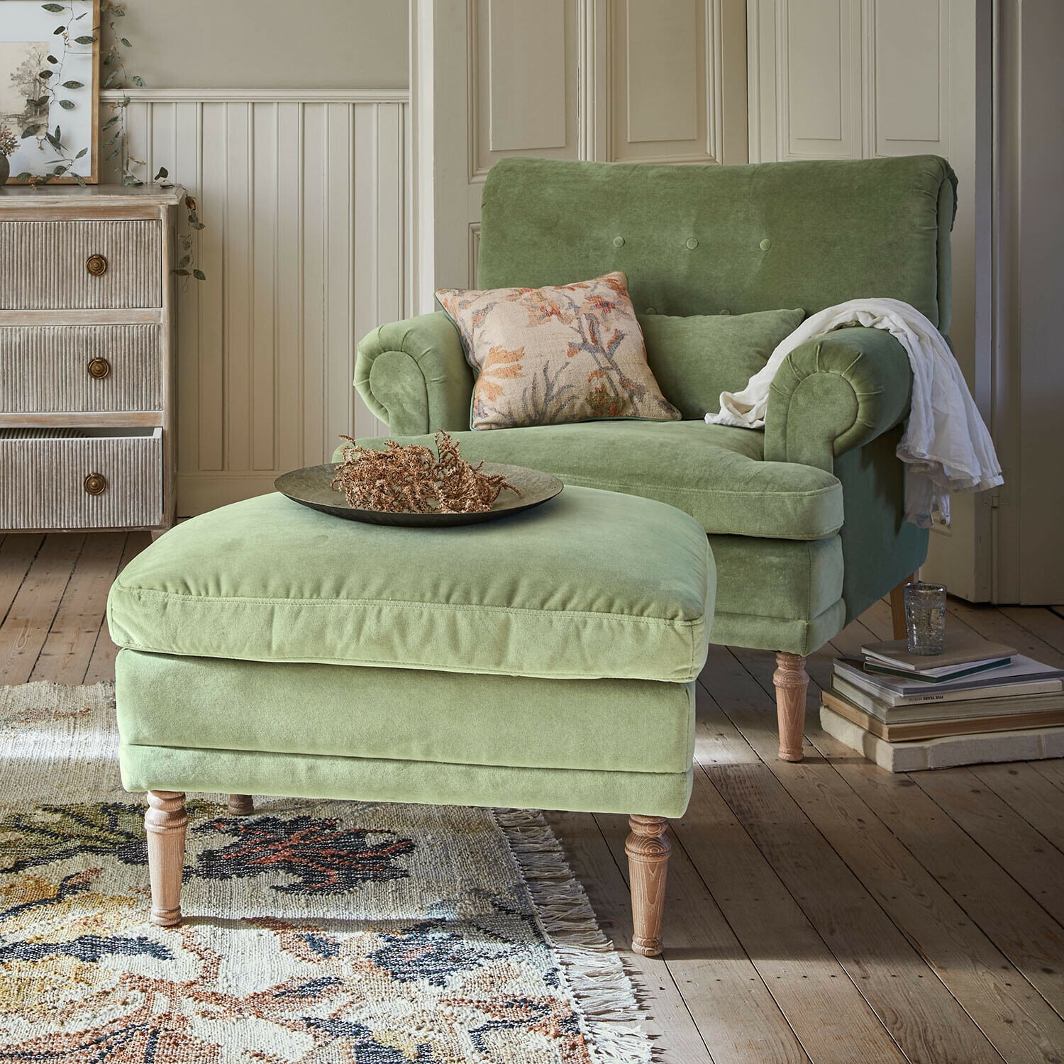 Fauteuil avec repose-pieds Éclat Émeraude Fauteuil vert en velours avec repose-pieds sur pieds en bois dans un salon chaleureux avec tapis