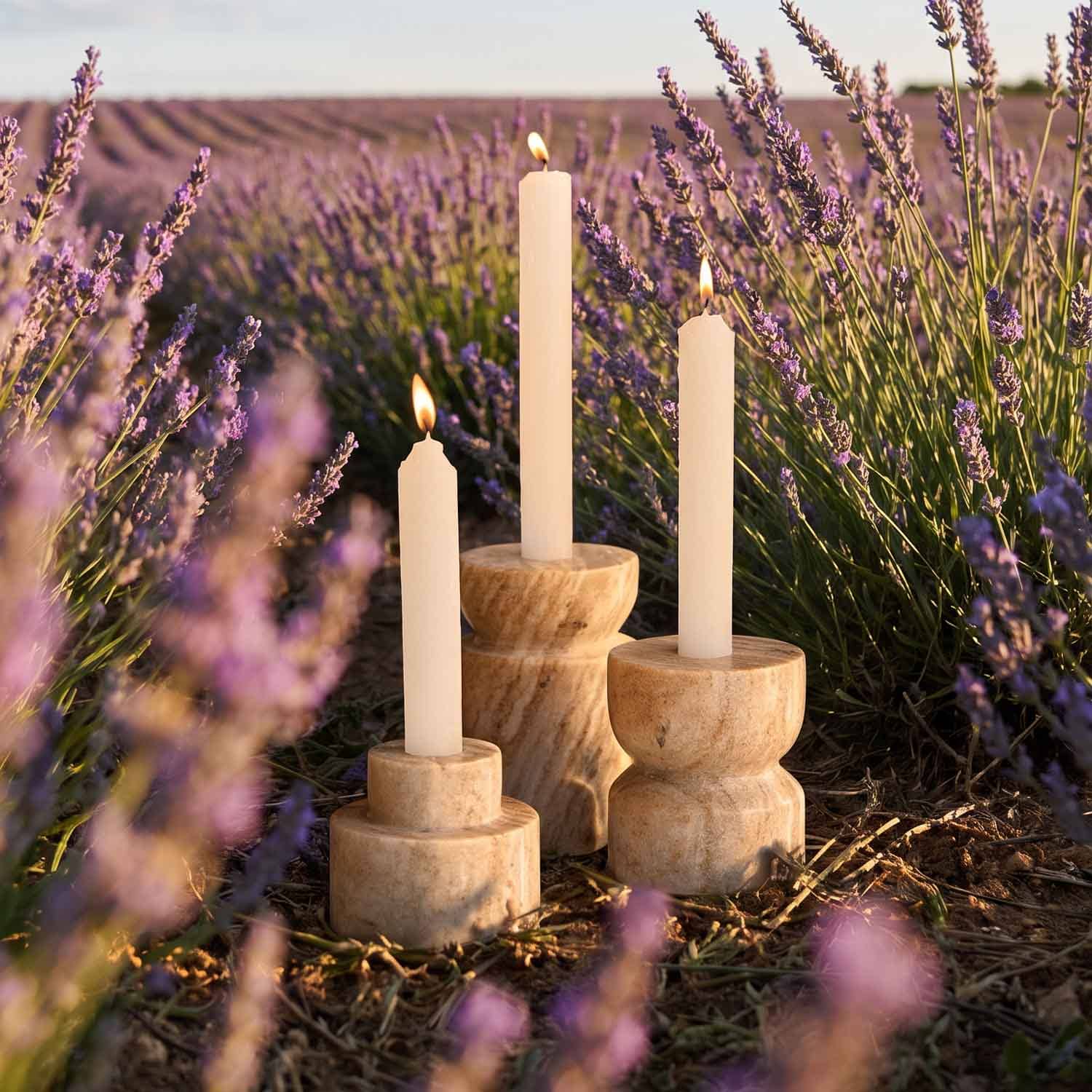 Drie crèmekleurige kaarsen in natuurlijke houten kandelaars op een lavendelveld bij zonsondergang