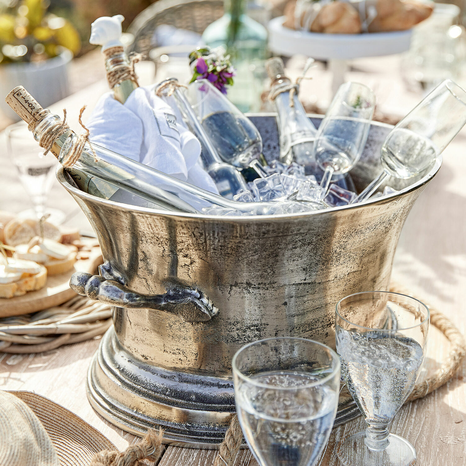 Champagnekoeler Cerisé Metalen ijsemmer met flessen en champagneglazen op een zonnige houten tafel