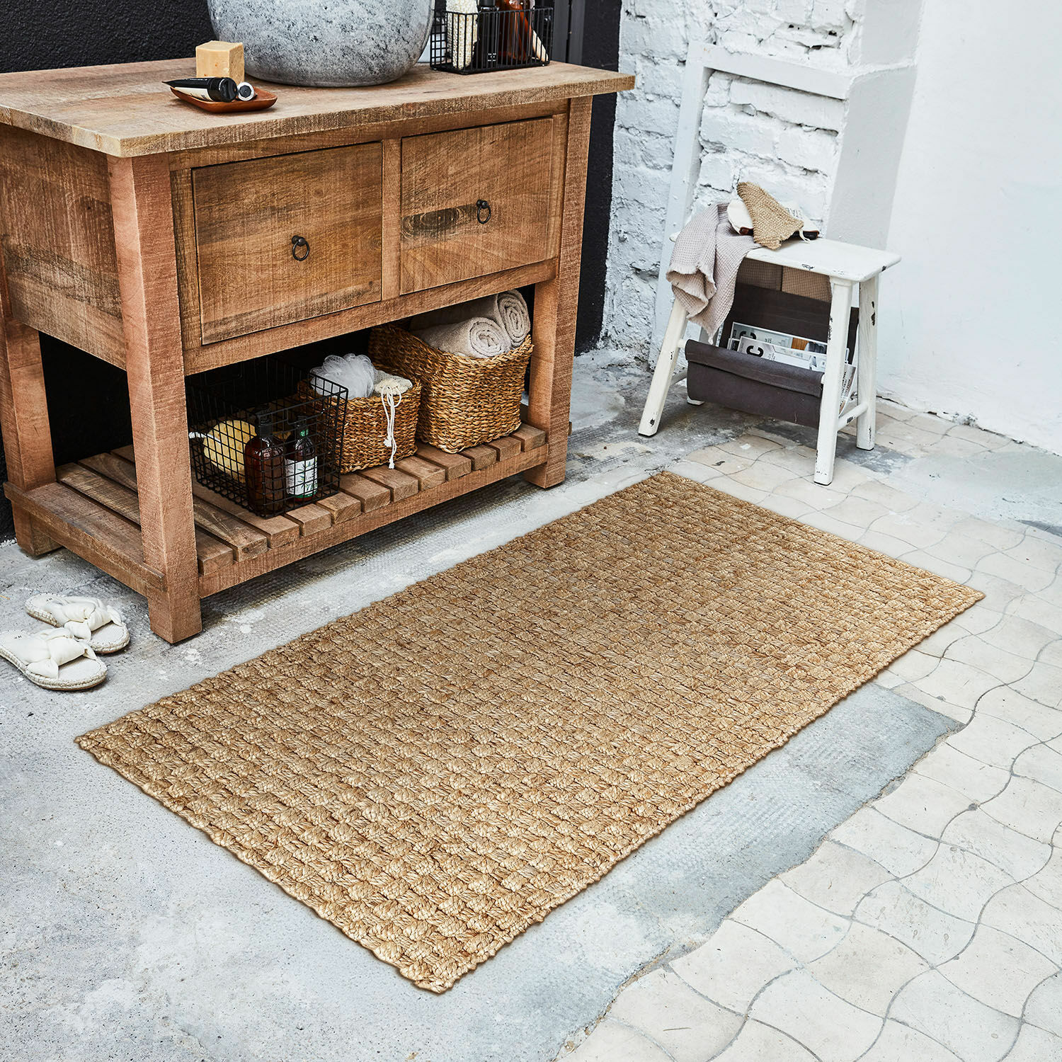 Loper Daoukro Beige vloerkleed van natuurlijke jute op de vloer naast een houten kast en een witte kruk