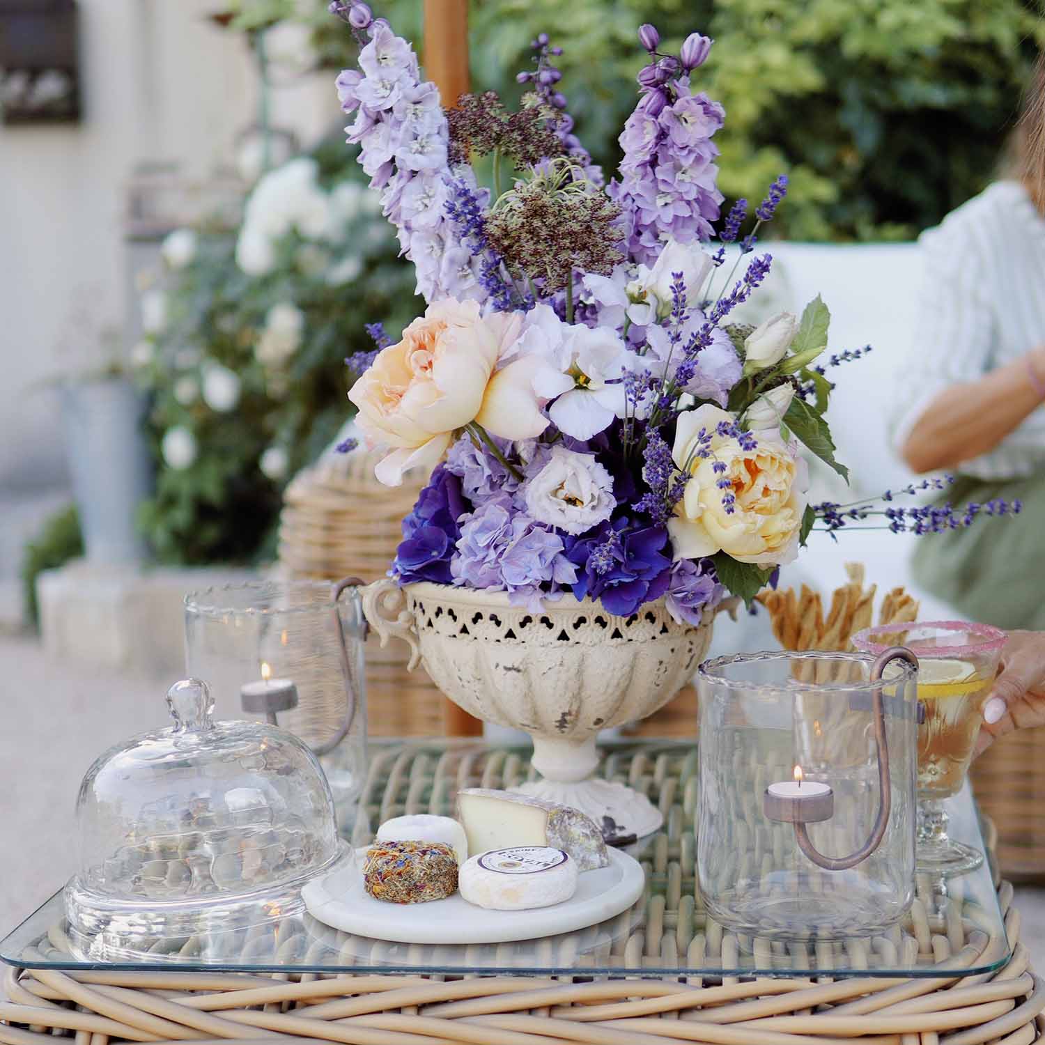 Bouquet de fleurs violettes et crème dans un vase en céramique blanche sur une table en verre avec bougies et fromage