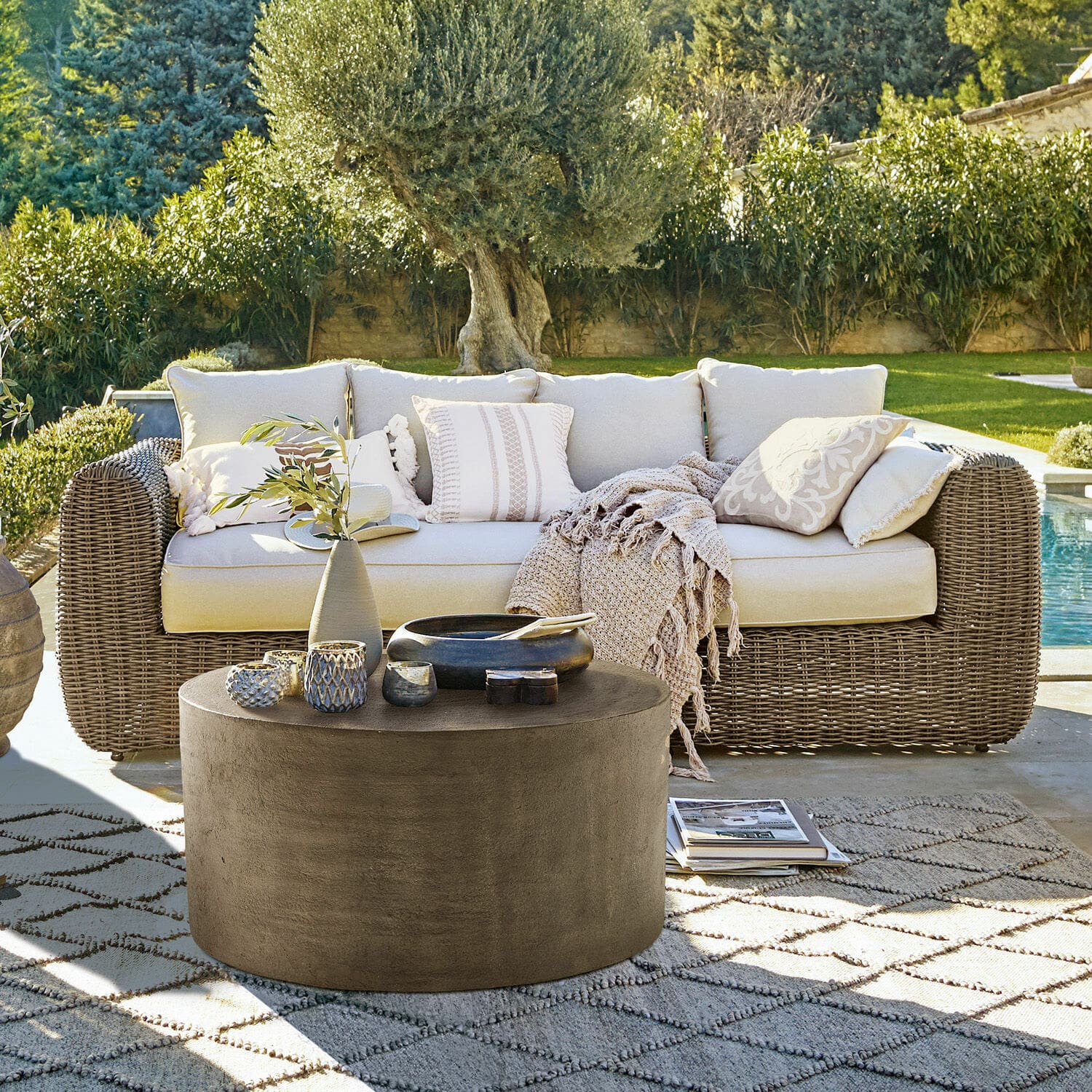 Bank Bogdanne Beige rotan loungeset met kussens en ronde betonnen salontafel op patroon vloerkleed buiten