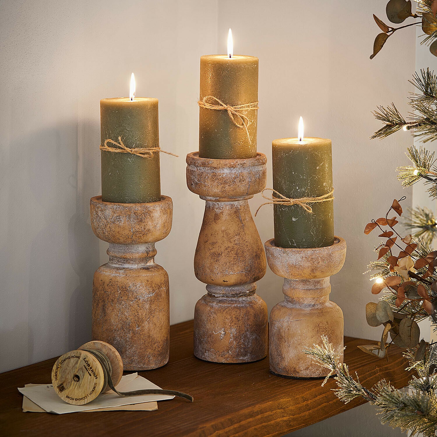 Set de 3 bougeoirs Talona Trois bougeoirs rustiques en bois avec bougies vertes et ficelle sur une étagère en bois décorative