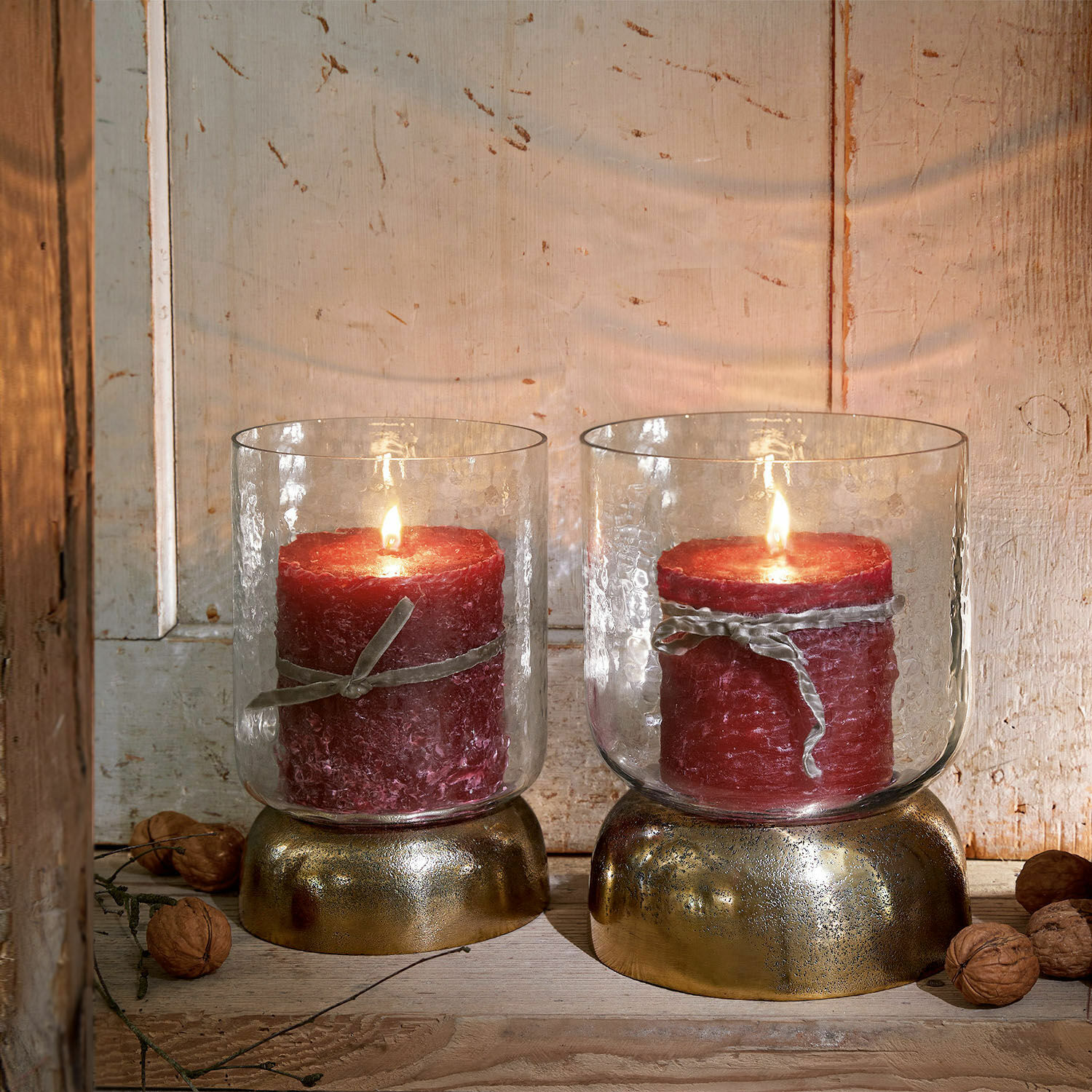 Deux bougies rouges dans des verres avec socles dorés sur fond en bois rustique