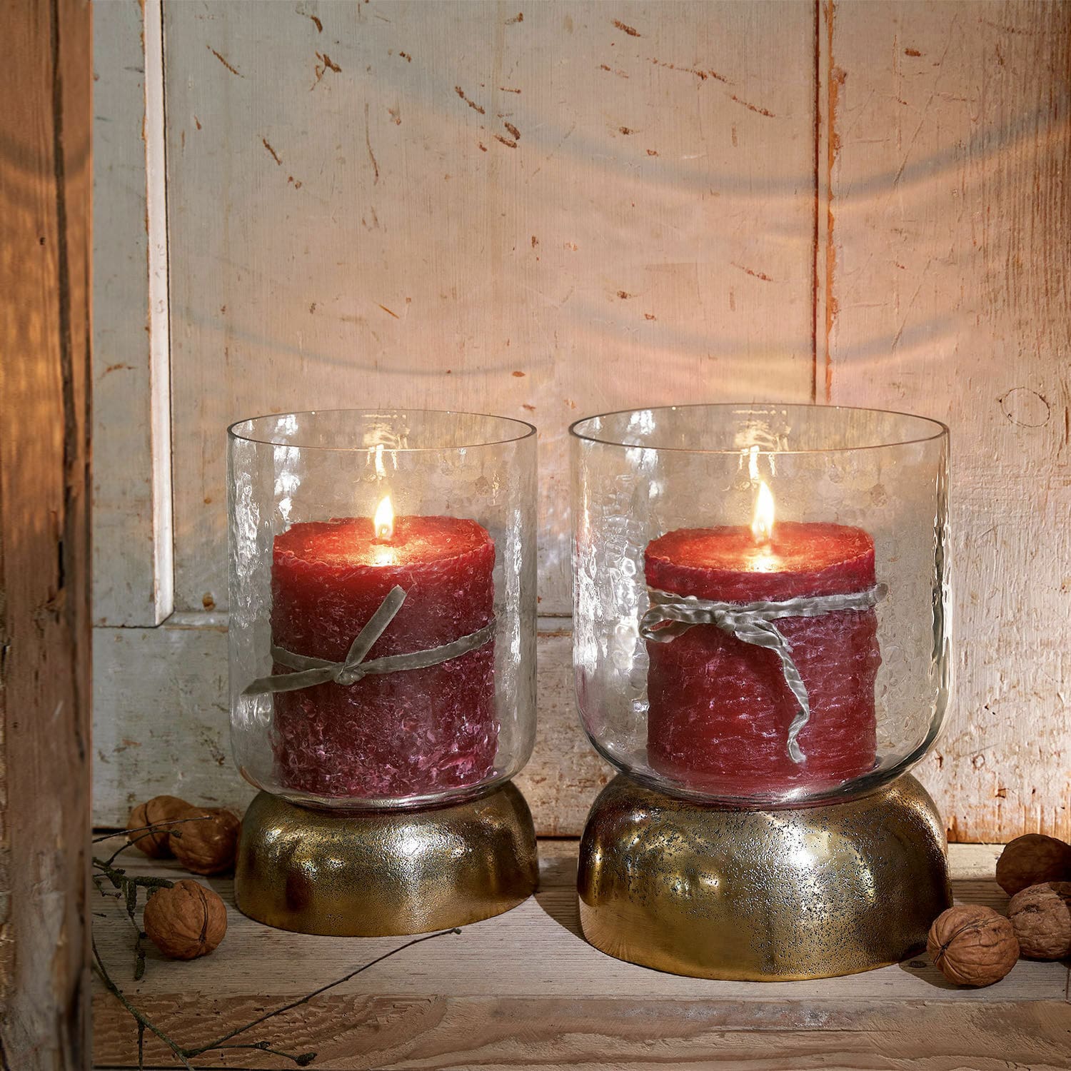 Lot de 2 photophores Biserre Deux bougies rouges dans des verres avec socles dorés sur fond en bois rustique