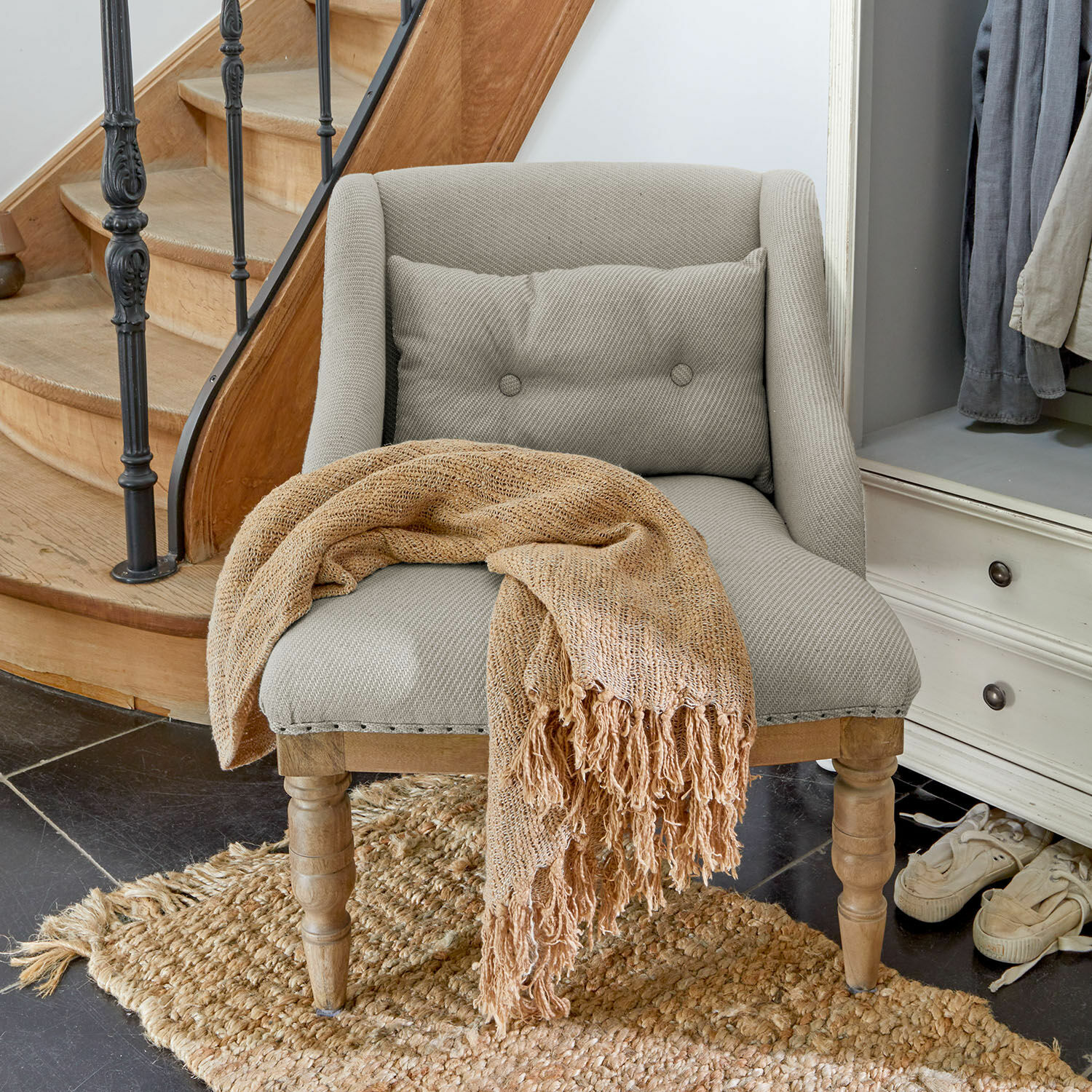 Fauteuil Lac d'Or Grijze gestoffeerde stoel met houten poten en beige gebreide deken op jute vloerkleed