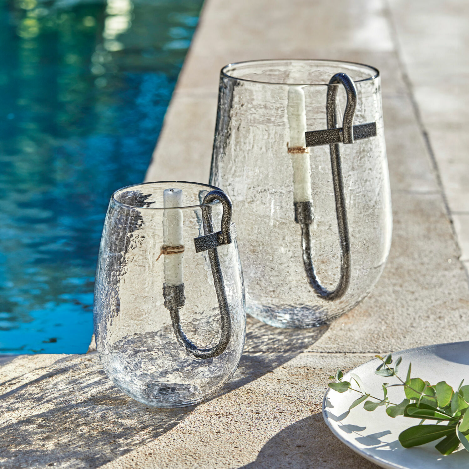 Lanterne en verre avec poignée en métal et bougie blanche près de la piscine, décoration extérieure