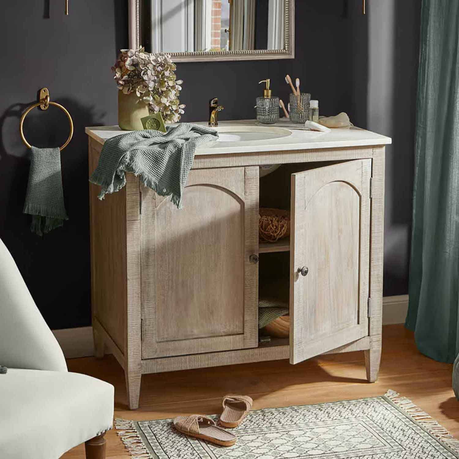 Meuble de salle de bain en bois clair avec lavabo blanc et robinet doré, serviette verte et décorations