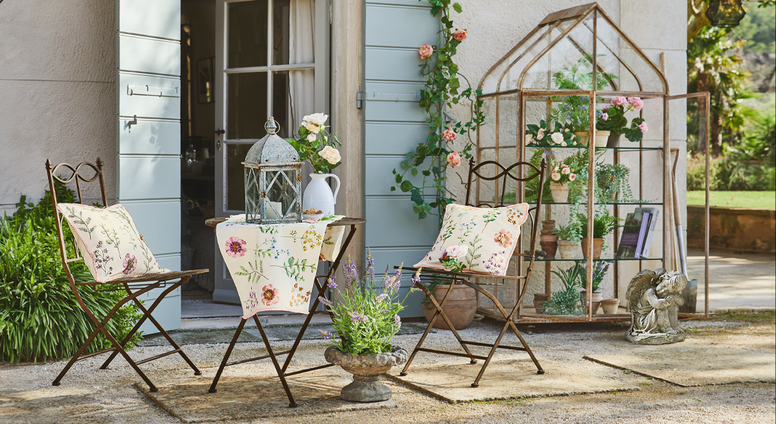 Ensemble de jardin en métal avec chaises et table décorée d'une nappe fleurie sur terrasse avec plantes