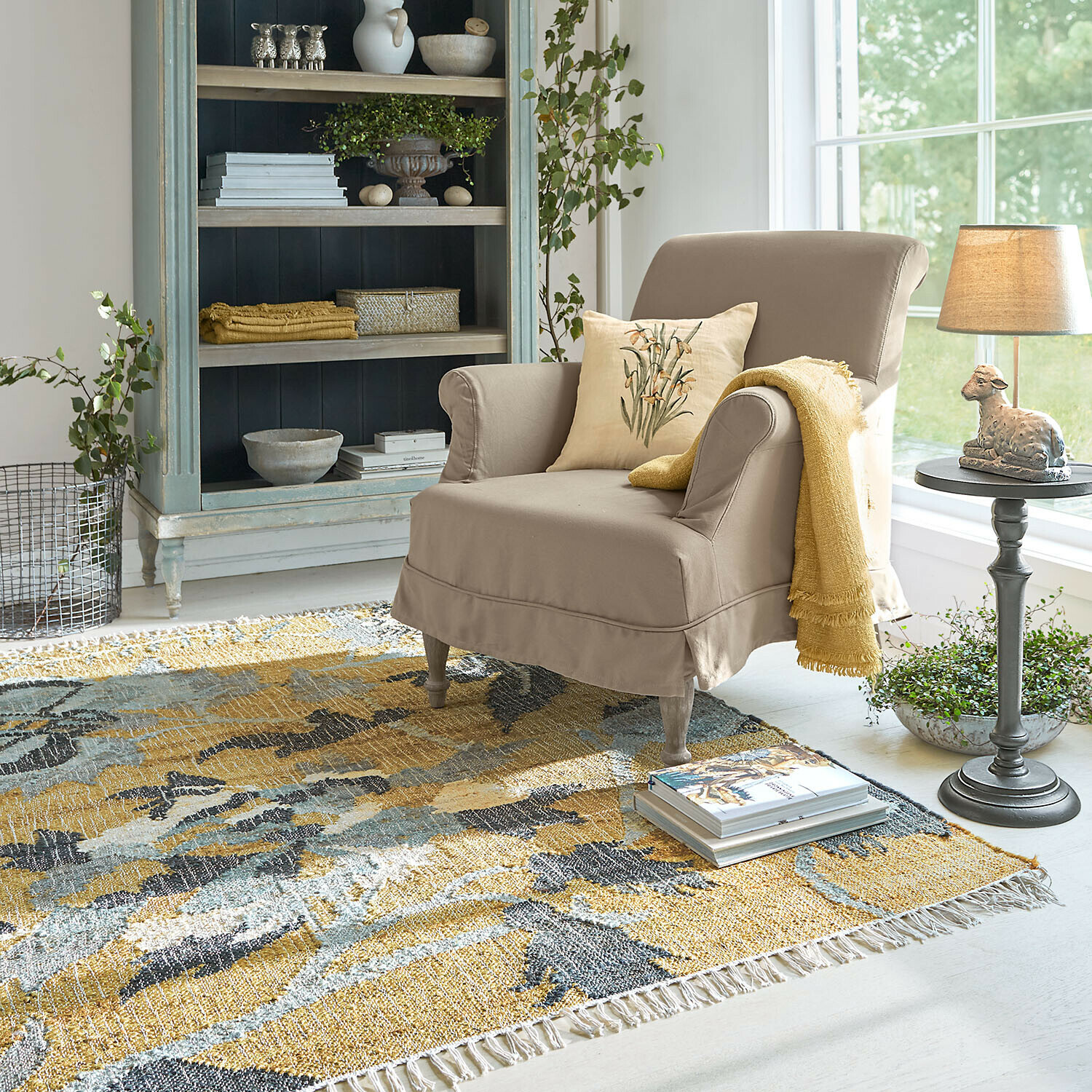 Vloerkleed Ornelless Beige fauteuil met kussen en gele deken op kleurrijk vloerkleed in lichte woonkamer met kast
