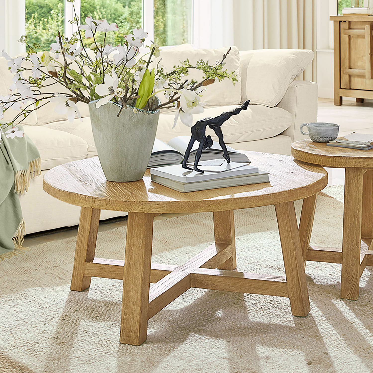 Table basse Gorivel Table basse ronde en chêne naturel avec décoration et livres dans un salon lumineux et cosy
