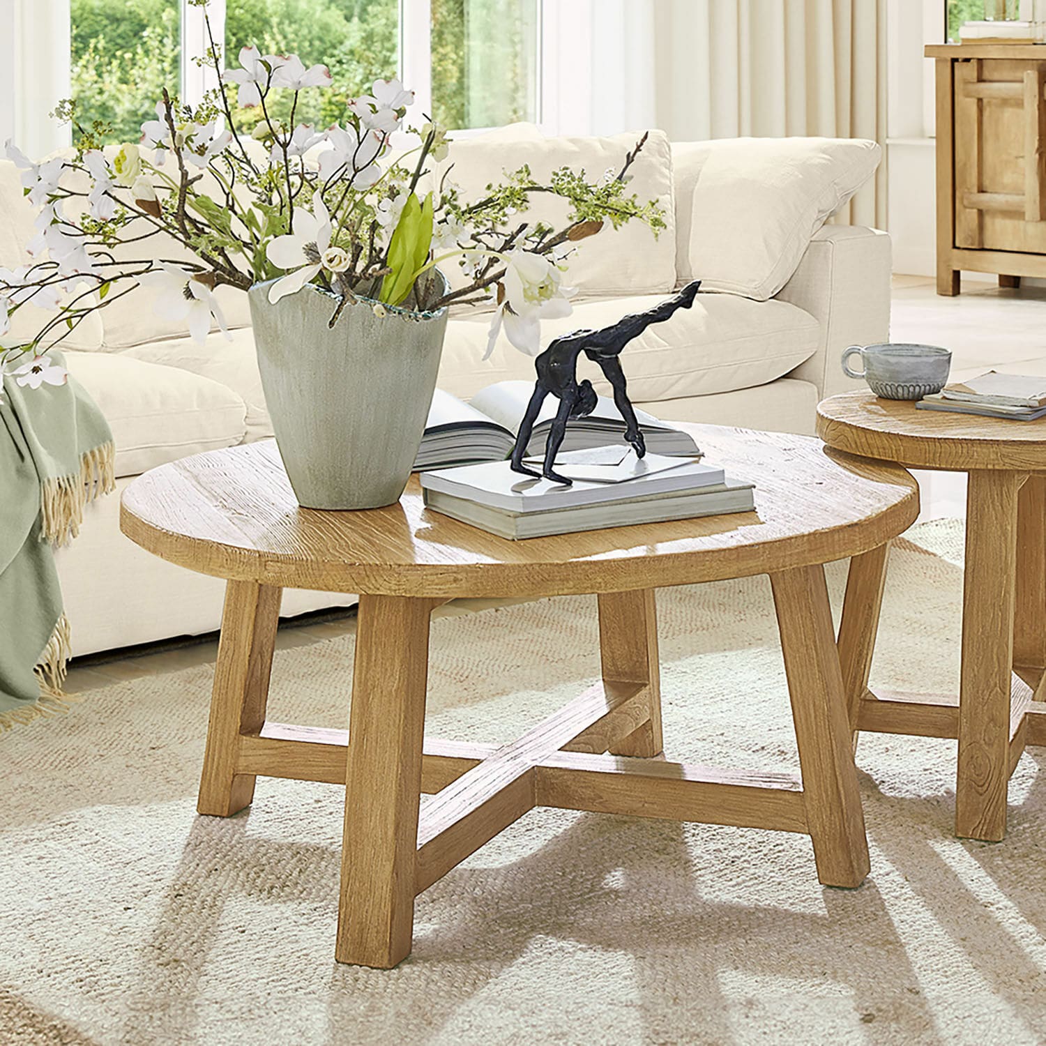 Table basse Gorivel Table basse ronde en chêne naturel avec décoration et livres dans un salon lumineux et cosy