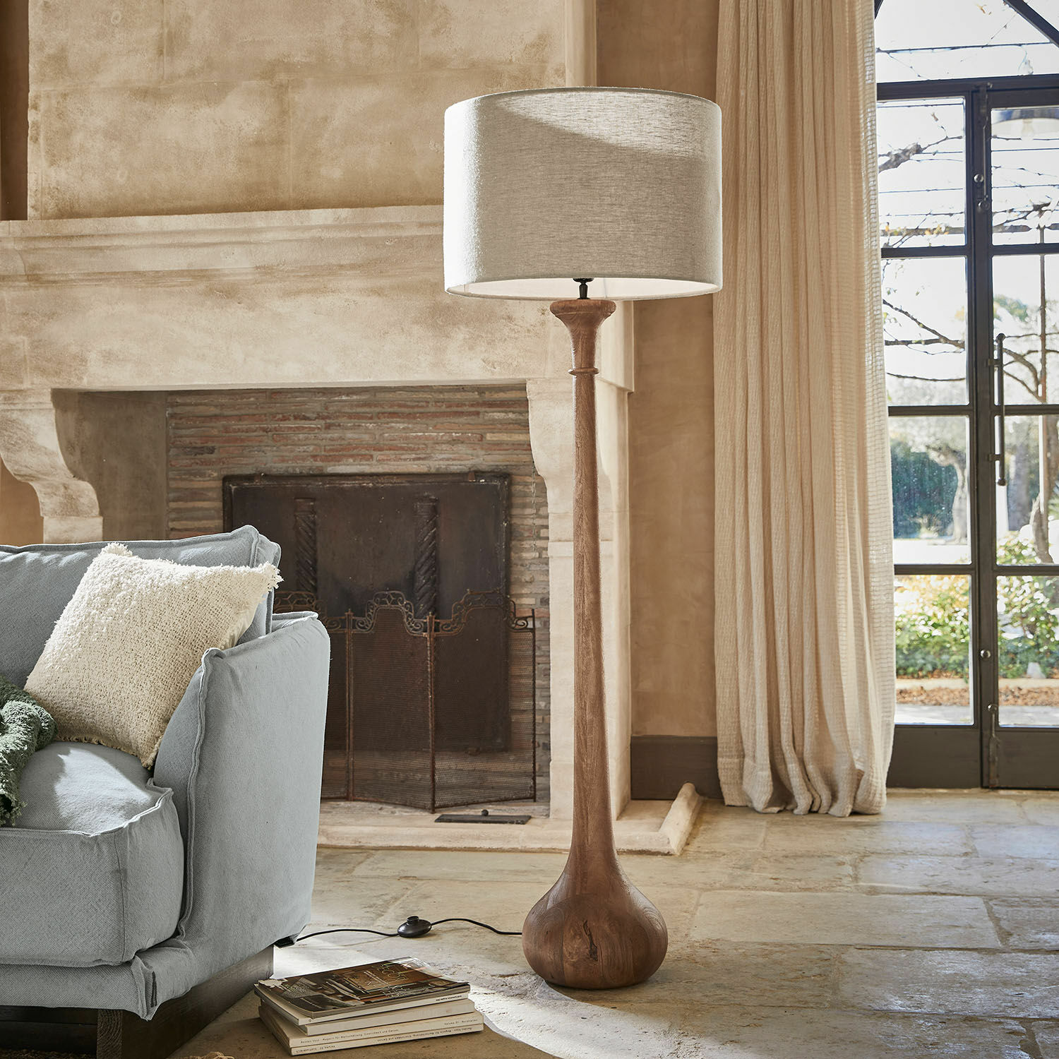 Staande lamp Andrées Vloerlamp met houten voet en beige kap in een gezellige woonkamer met open haard en blauwe bank