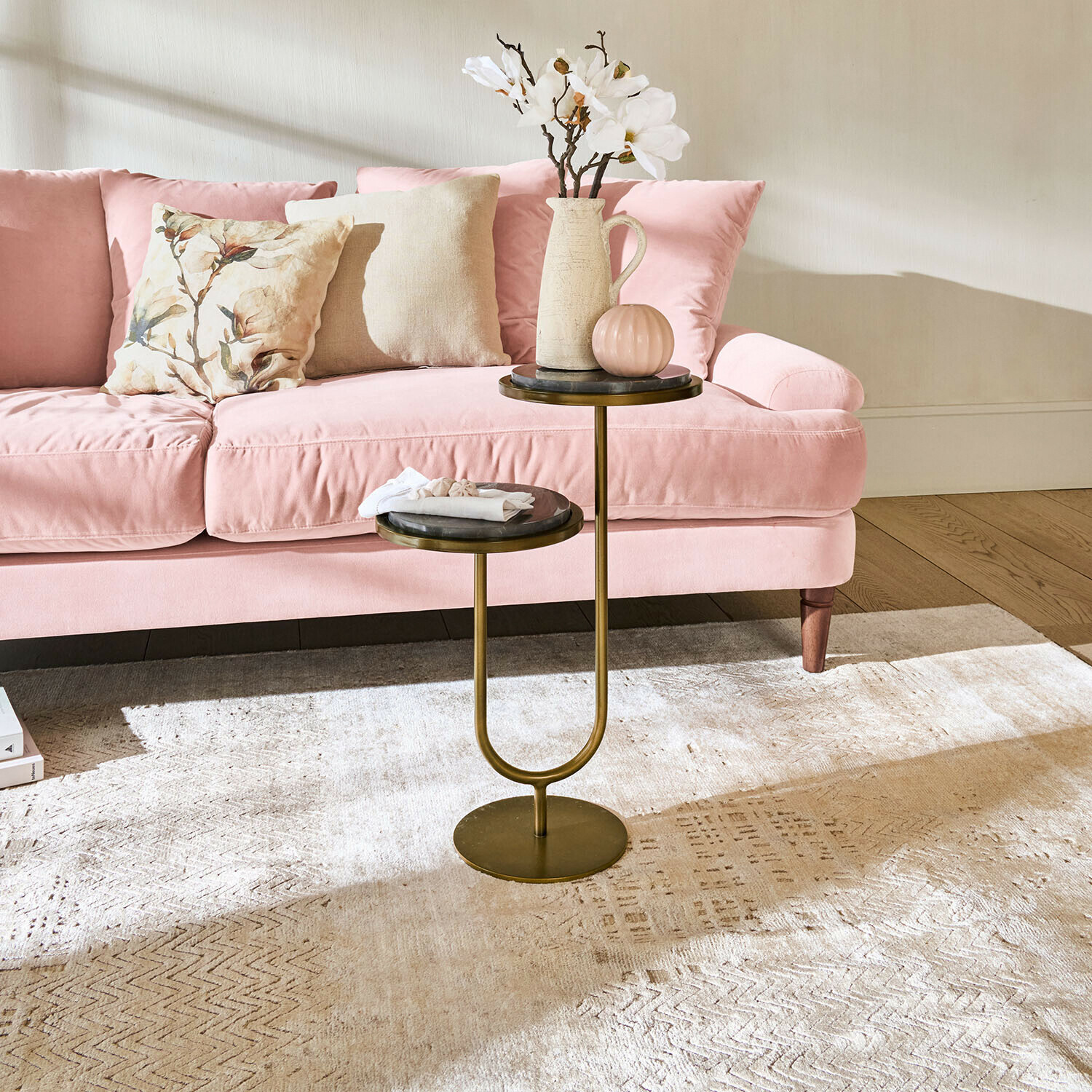 Table d'appoint double en métal avec plateaux en marbre devant un canapé rose dans un salon lumineux