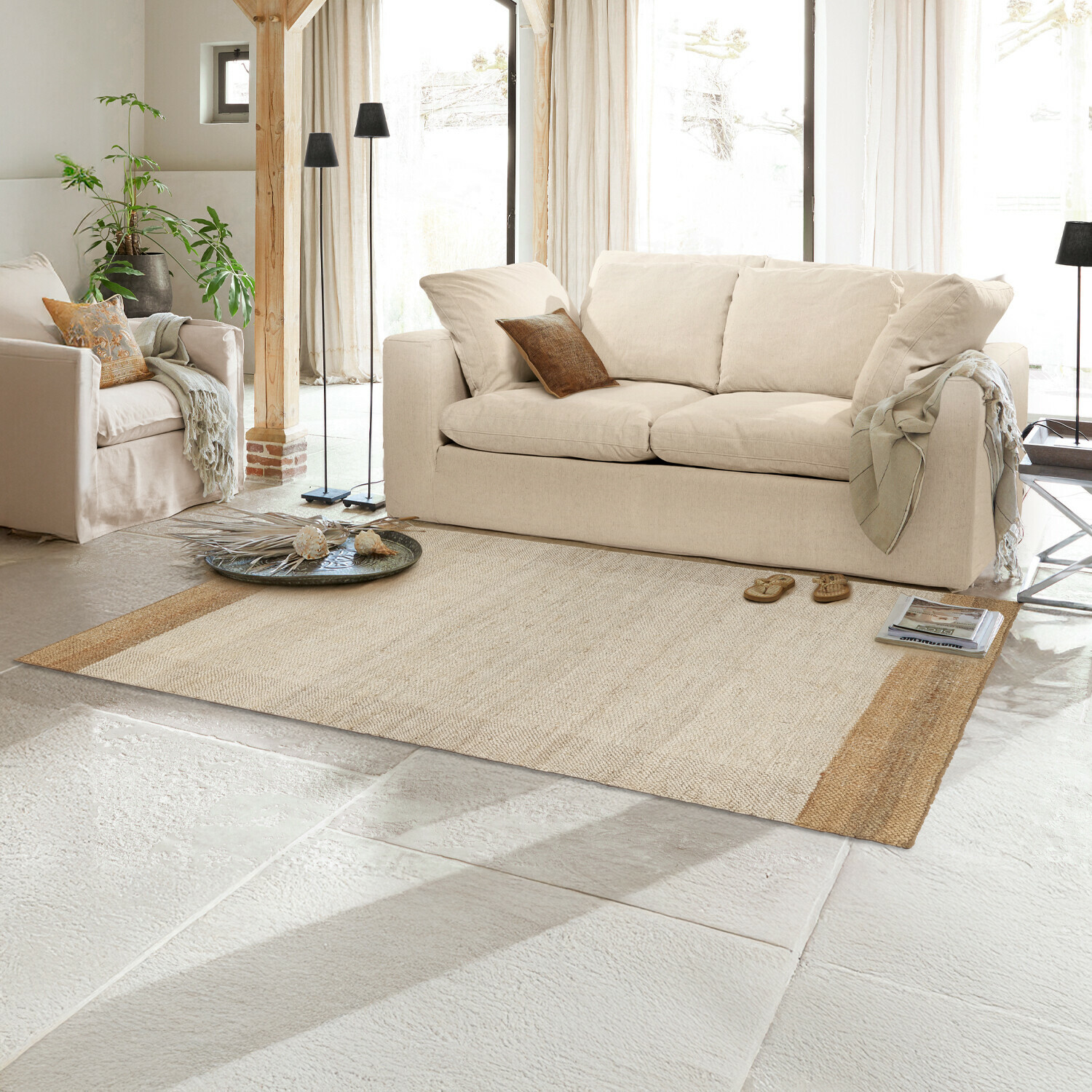Vloerkleed Estelune Beige vloerkleed van natuurlijke vezels in lichte woonkamer met crèmekleurige bank en decoratie