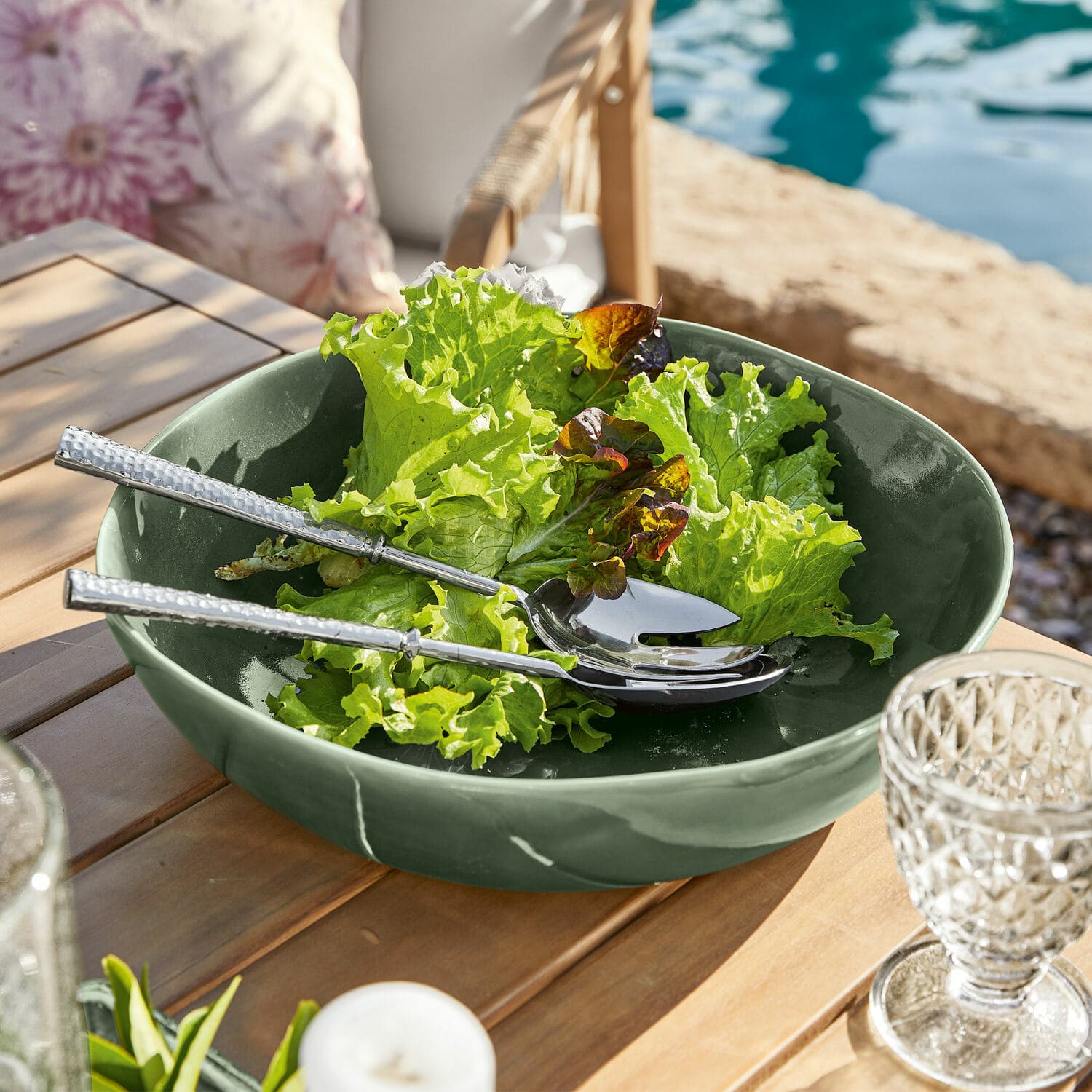 Saladier en céramique verte avec salade et couverts en argent sur table en bois en extérieur