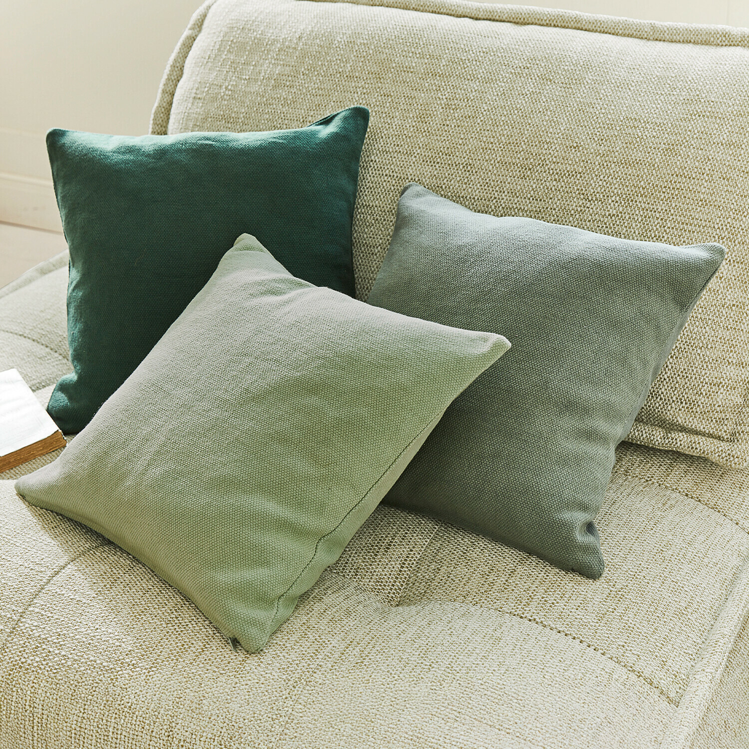 Lot de 3 housses de coussins Alienor Trois coussins décoratifs verts en tissu sur un canapé beige pour salon moderne