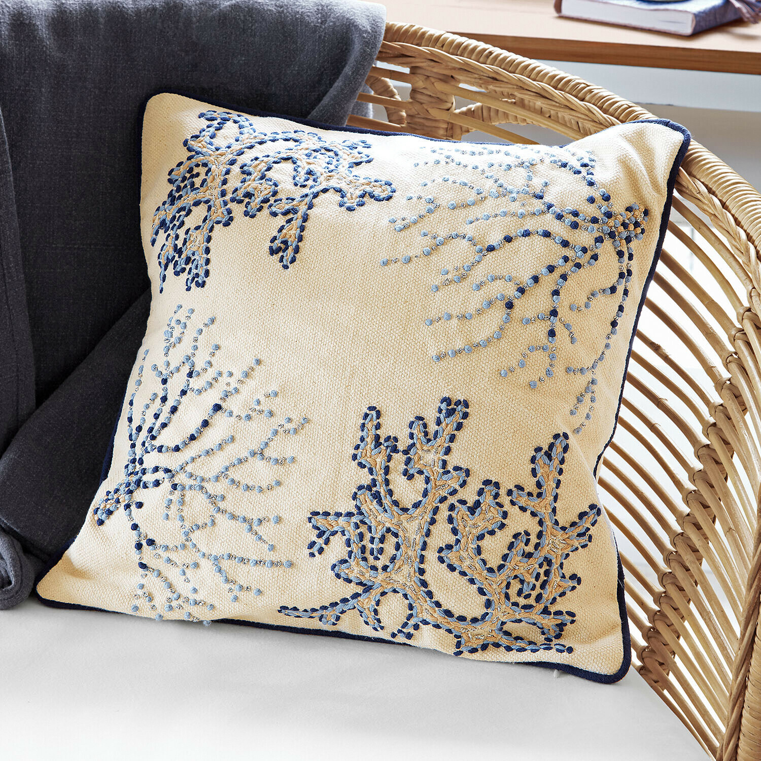 Kussenhoes Whitmere Beige sierkussen met blauwe borduursels en donkerblauwe bies op rotan stoel