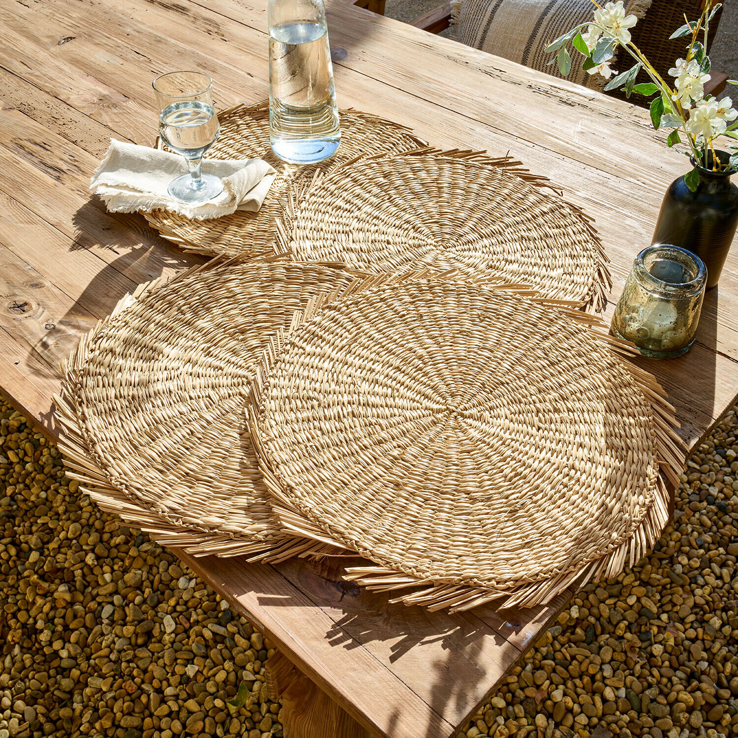Lot de 4 sets de table Nuviras Sets de table ronds en osier naturel posés sur une table en bois en extérieur