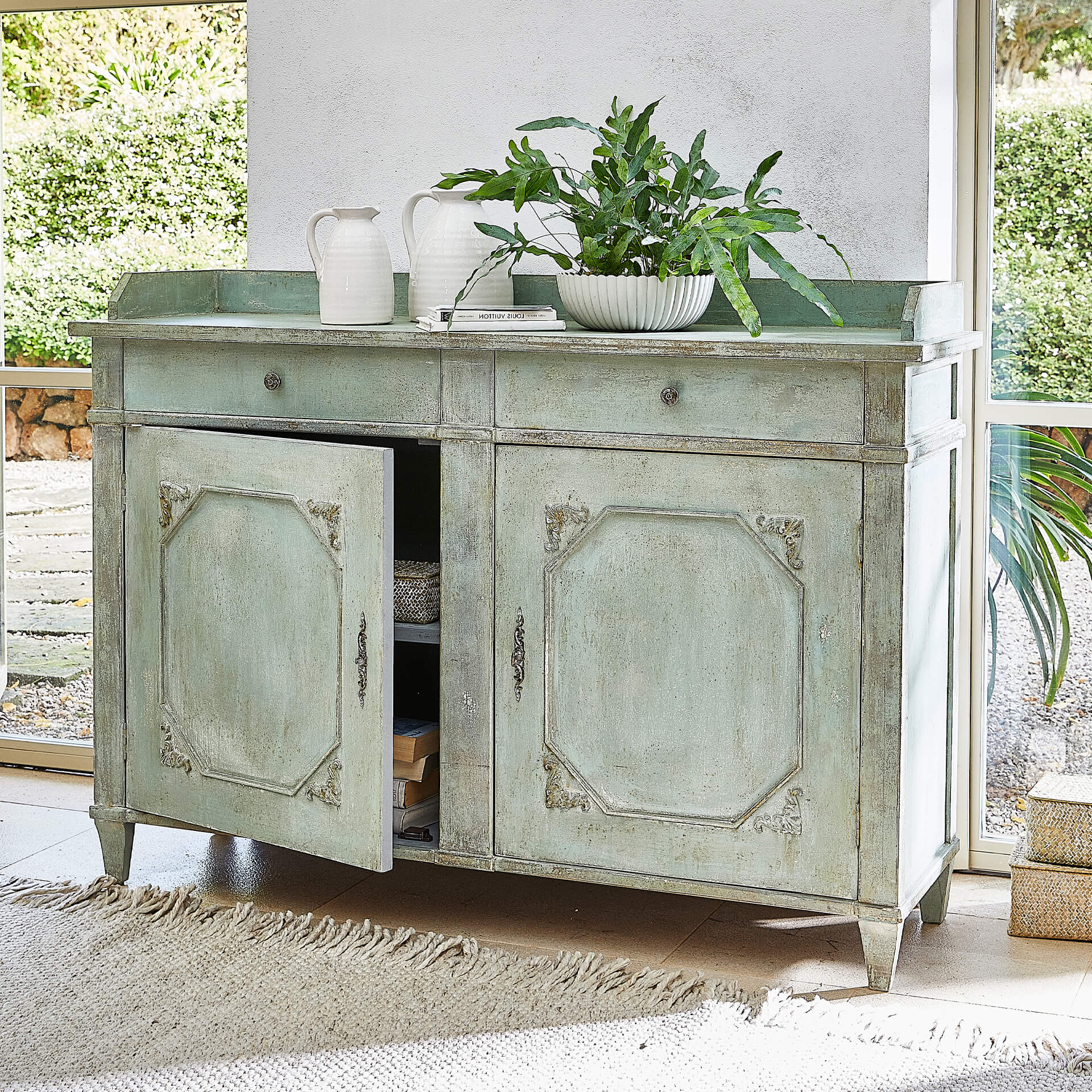 Buffet vert en bois avec deux tiroirs et portes décoratives dans un salon lumineux