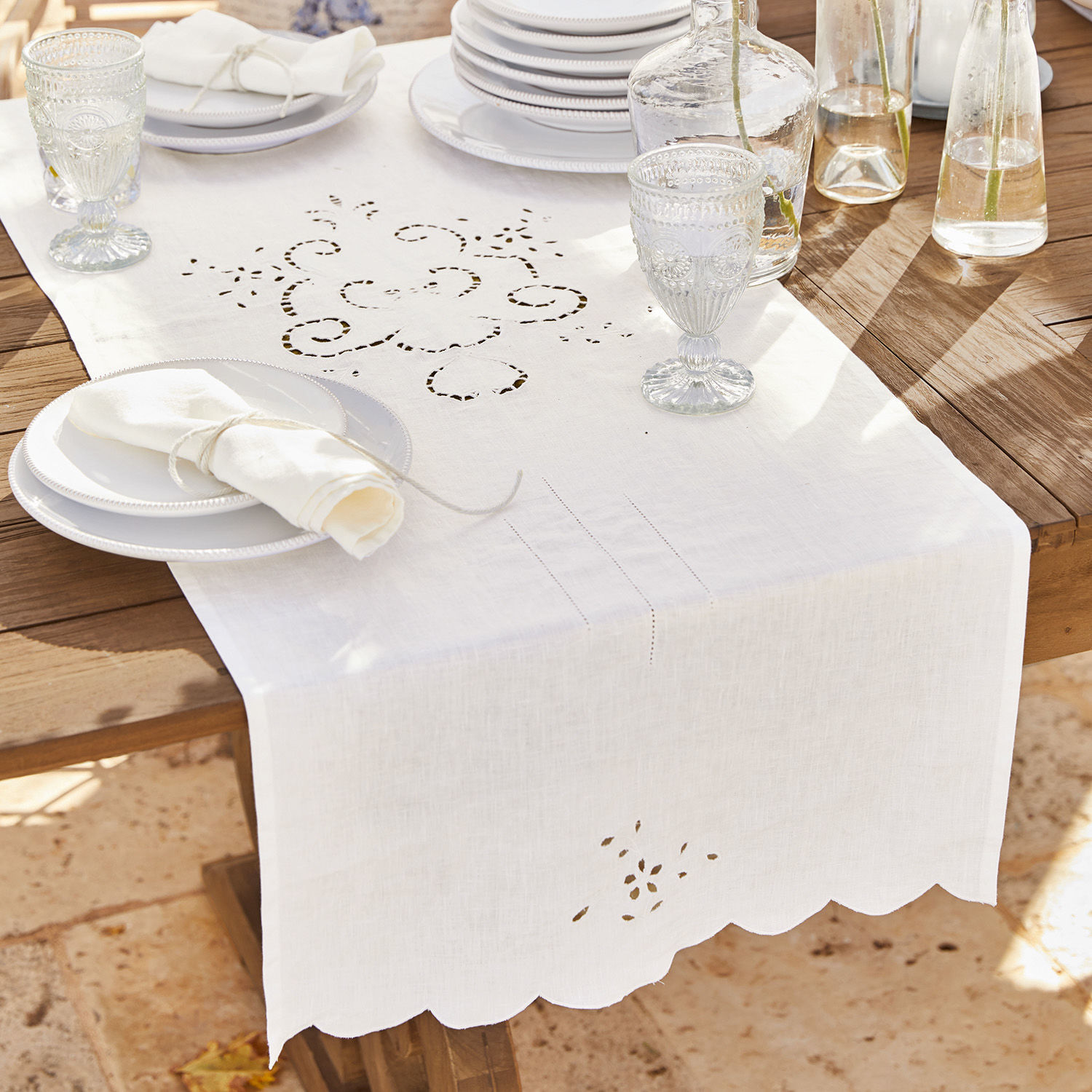 Chemin de table Kara Chemin de table en lin blanc avec motif ajouré sur table en bois avec vaisselle et verres