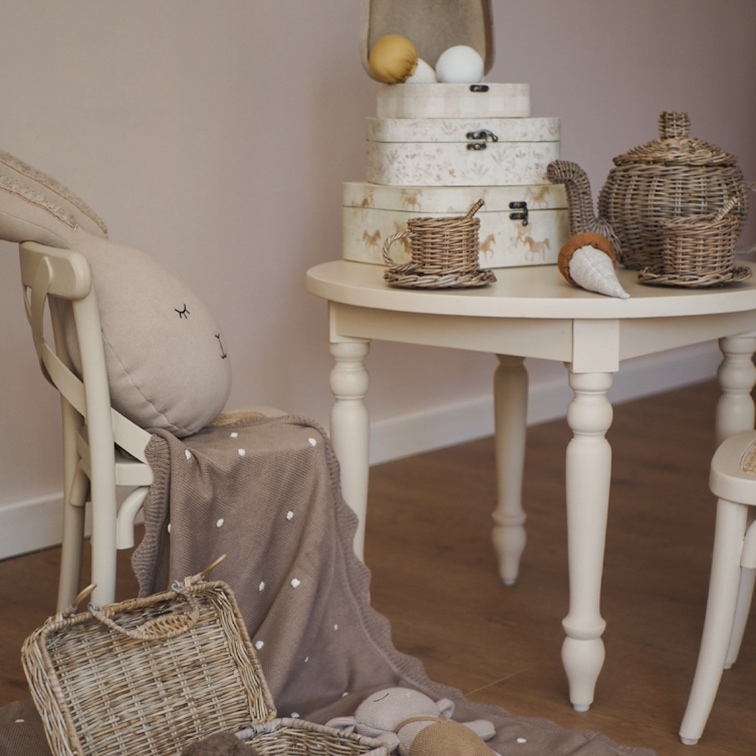 Beige tafel met rieten theeset en decoratieve dozen in een gezellige kinderkamer