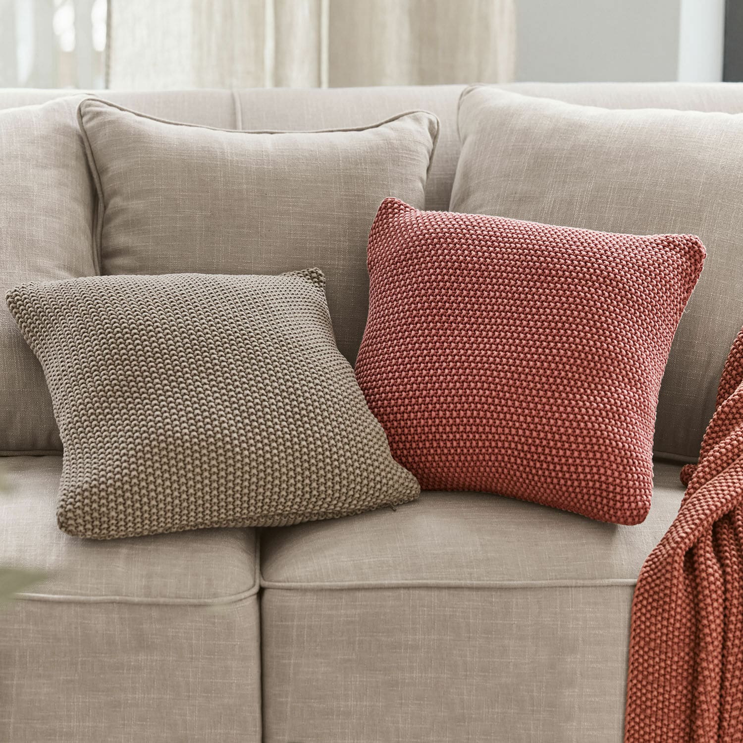 Deux coussins carrés en tricot beige et brique sur un canapé gris clair pour décoration intérieure