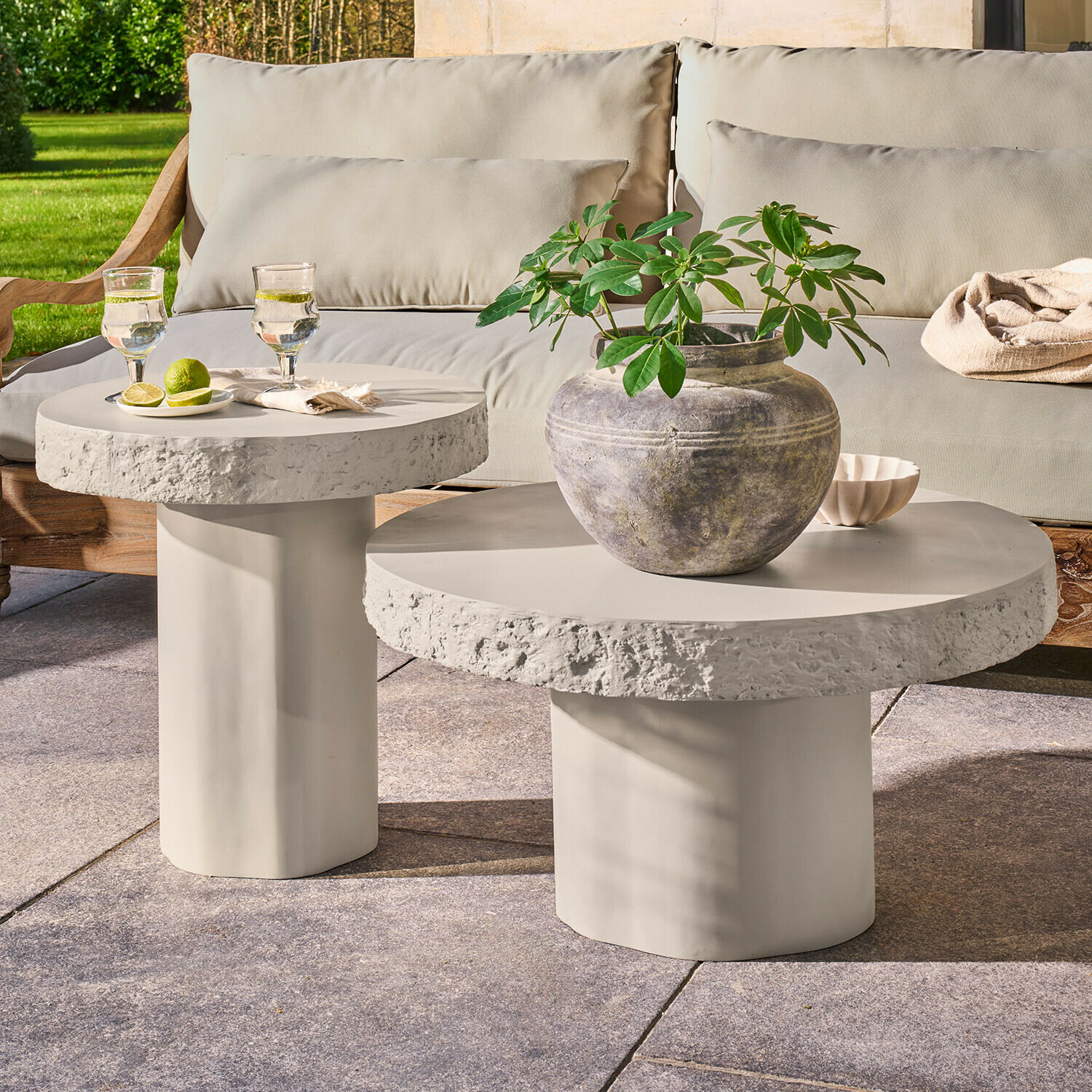 Lot de 2 tables basses Tivoliq Ensemble de deux tables basses rondes en béton gris clair sur terrasse avec plante et verres d'eau