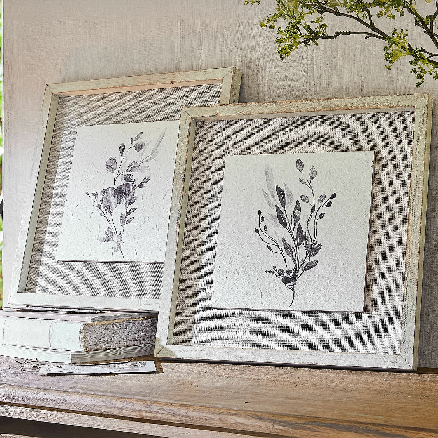 Afbeelding set van 2 Ylivane Twee rustieke schilderijen met zwart-witte plantenmotieven in houten lijsten op een houten tafel