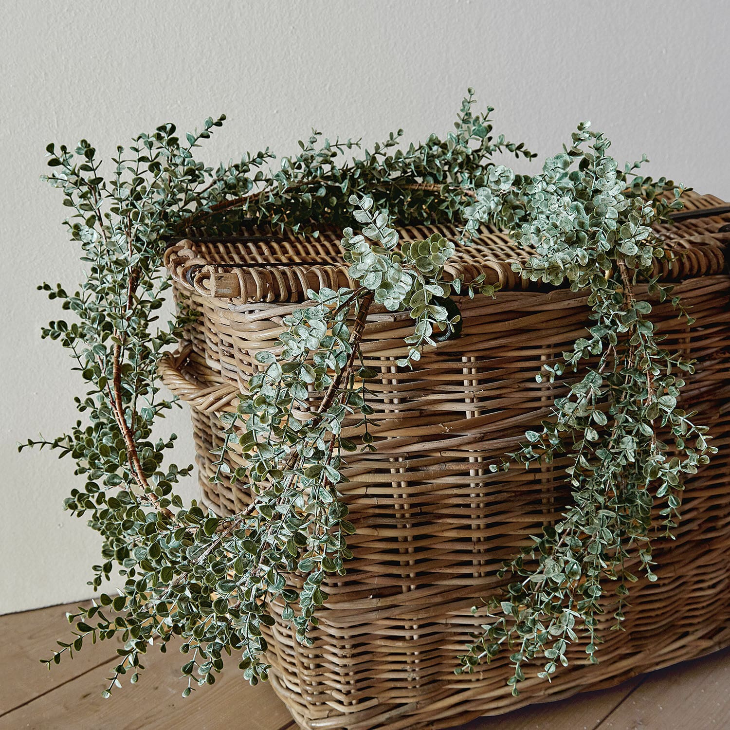 Guirlande Valerie Decoratieve krans van groene bladeren op een rieten mand op een houten vloer
