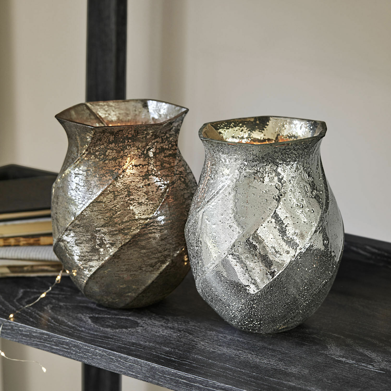 Lot de 2 photophores Tixovel Deux vases décoratifs en verre argenté et doré avec texture posés sur une étagère sombre