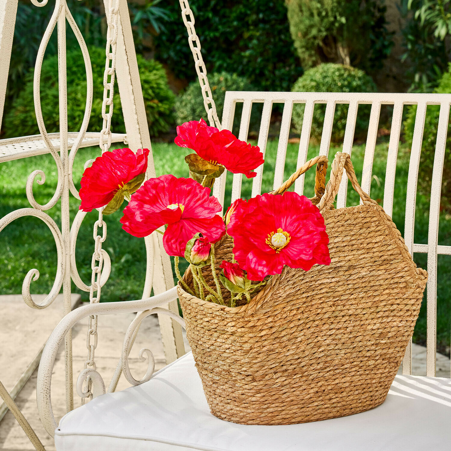 Panier tressé en herbe marine naturelle avec fleurs rouges sur chaise de jardin blanche