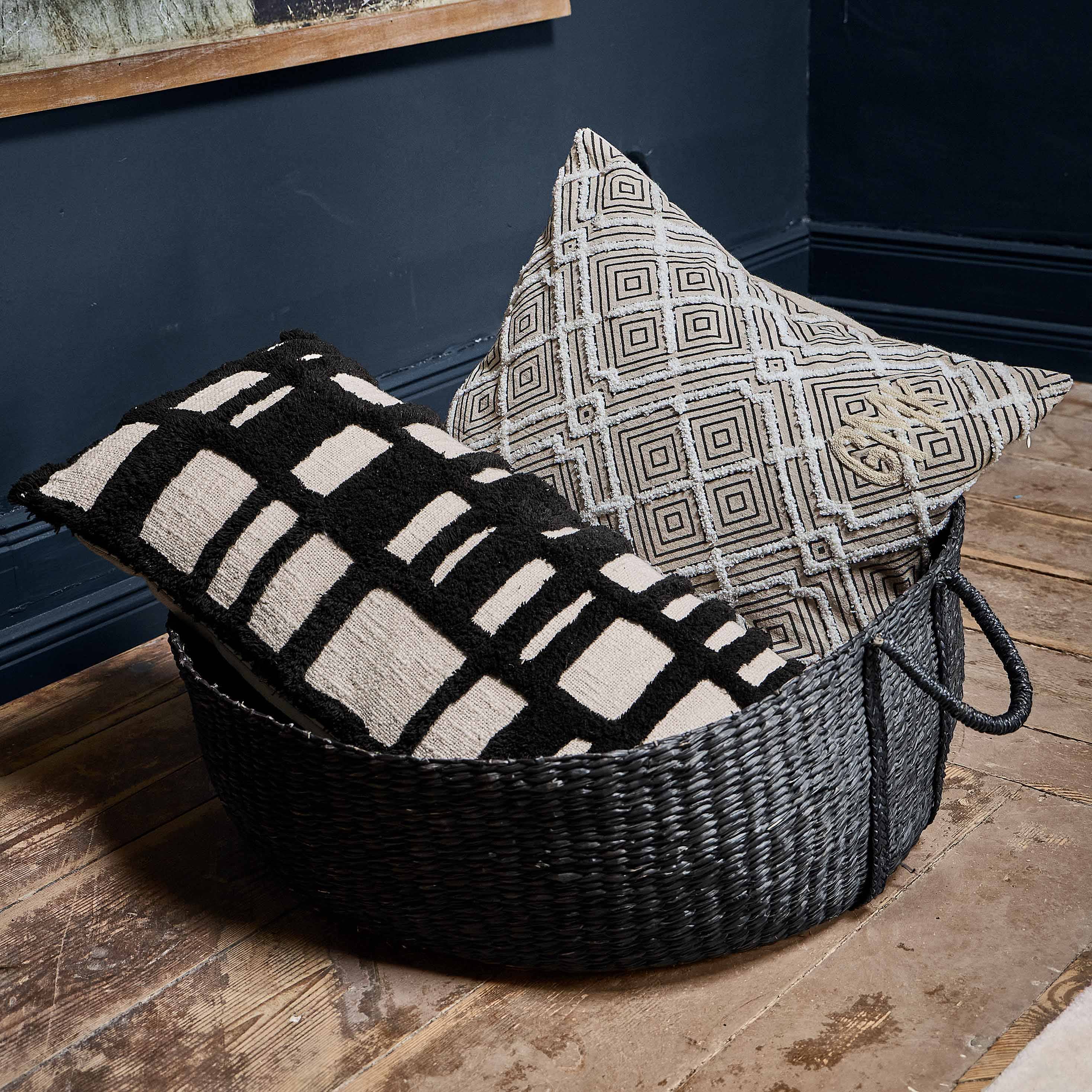Coussin décoratif noir et blanc à motif géométrique dans un panier sur un sol en bois