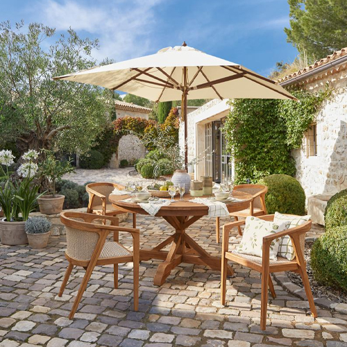 Houten tuintafel met parasol en vier stoelen op een stenen terras in de zon