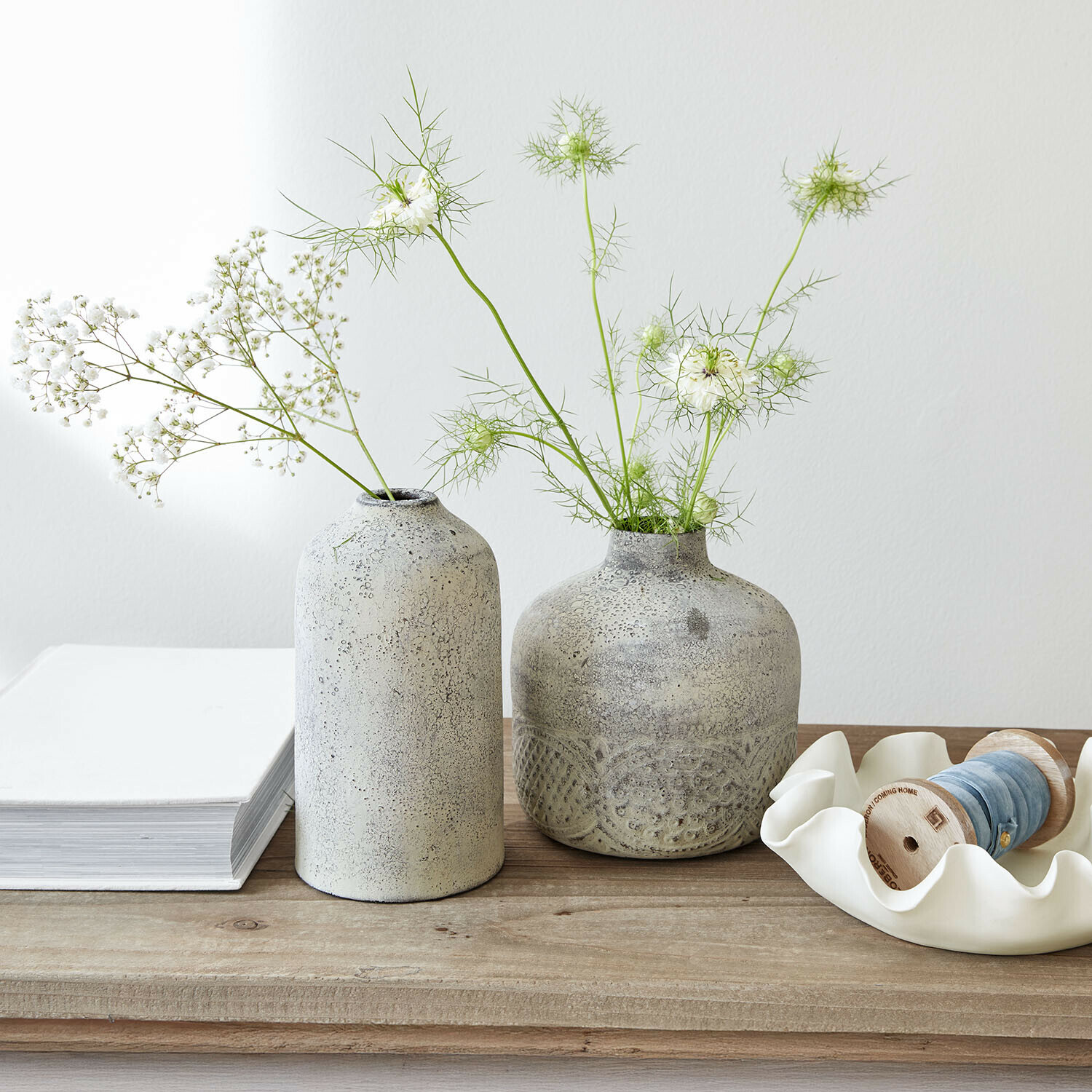 Deux vases en céramique grise avec des fleurs blanches délicates sur une table en bois clair
