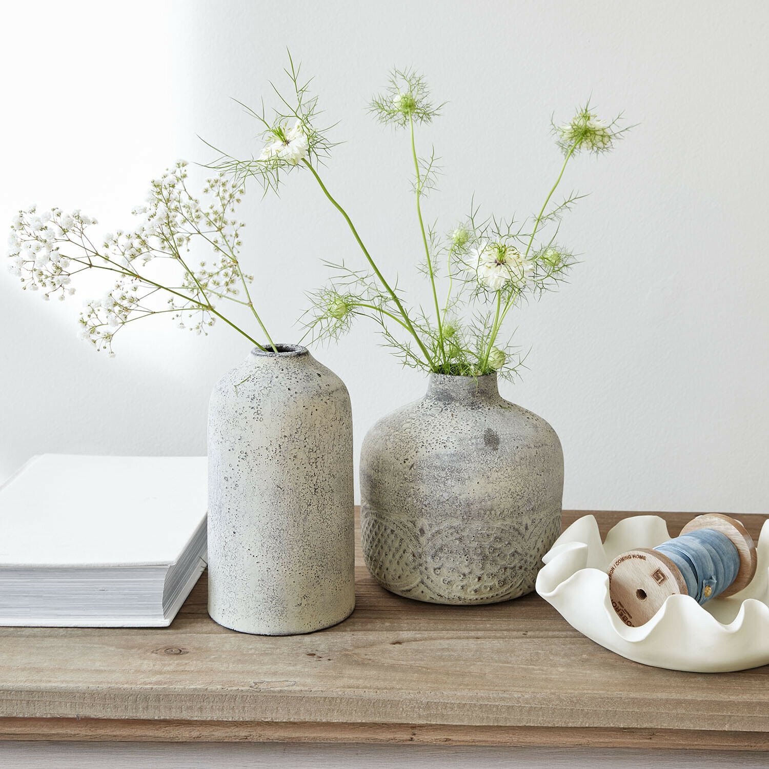 Deux vases en céramique grise avec des fleurs blanches délicates sur une table en bois clair