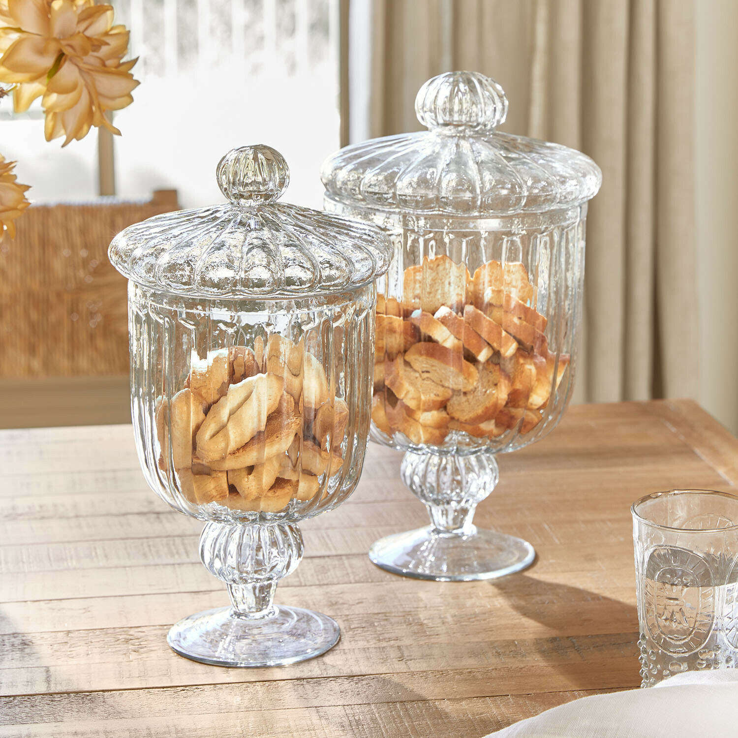 Glazen pot set van 2 Mélomiane Twee doorzichtige glazen potten met deksels gevuld met koekjes op een lichte houten tafel