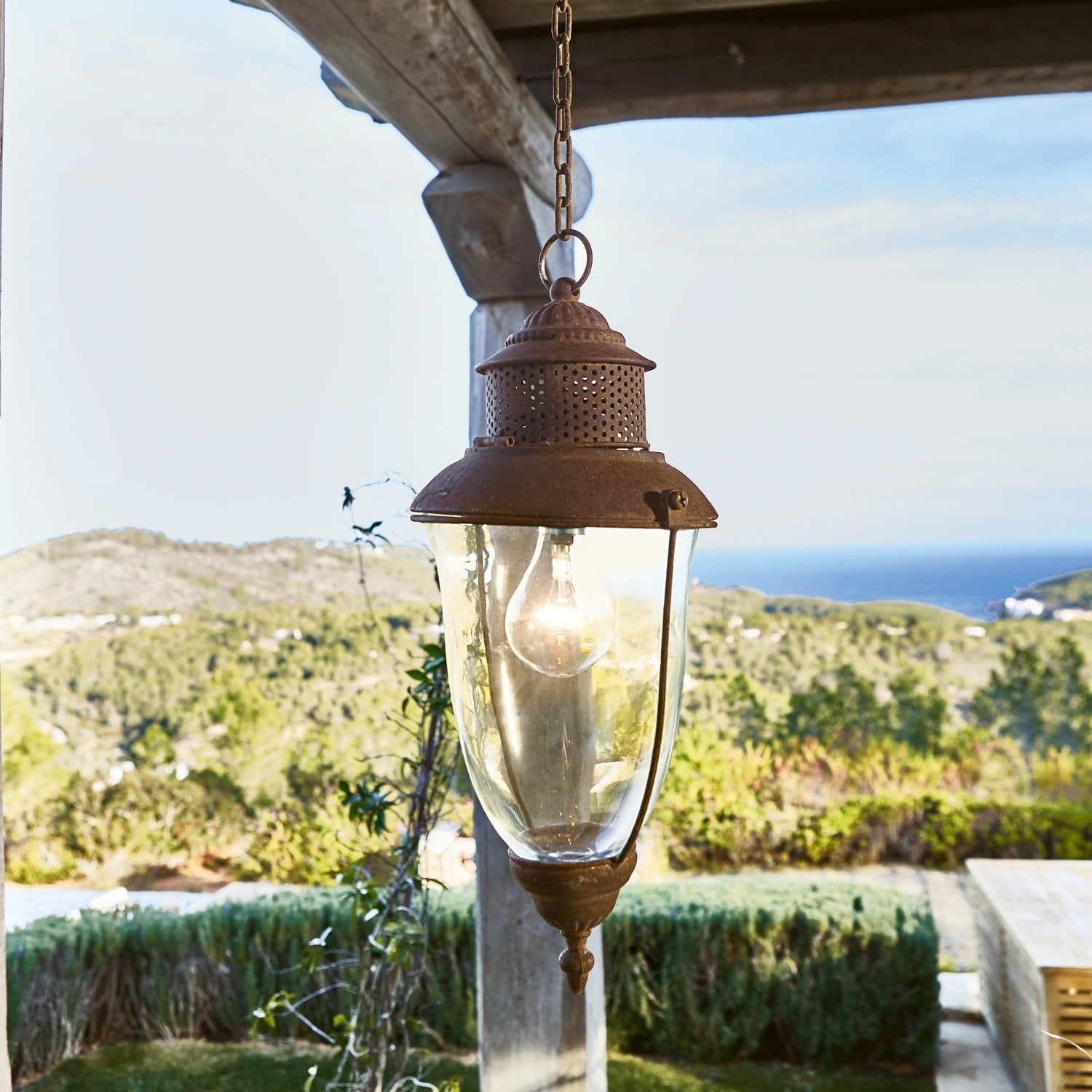 Hanglantaarn Floricia Hangende lamp van roestig metaal en glas met uitzicht op groene heuvels en zee op de achtergrond