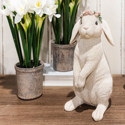 Lapin décoratif blanc avec couronne de fleurs sur table en bois près de pots avec fleurs blanches