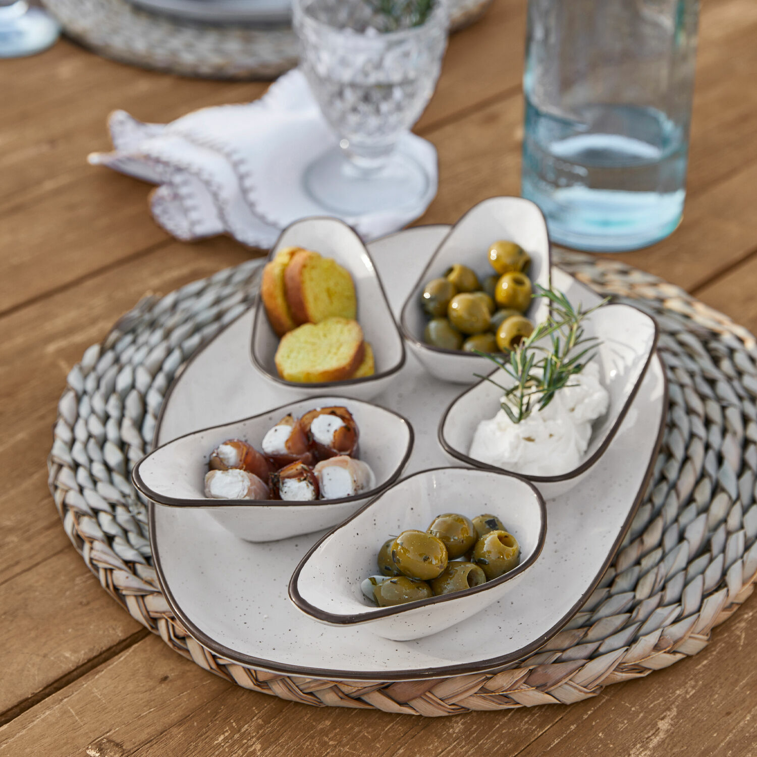Serveerschaal set van 6 Biarré Witte keramische schaaltjes met olijven en kaas op gevlochten onderzetter op houten tafel