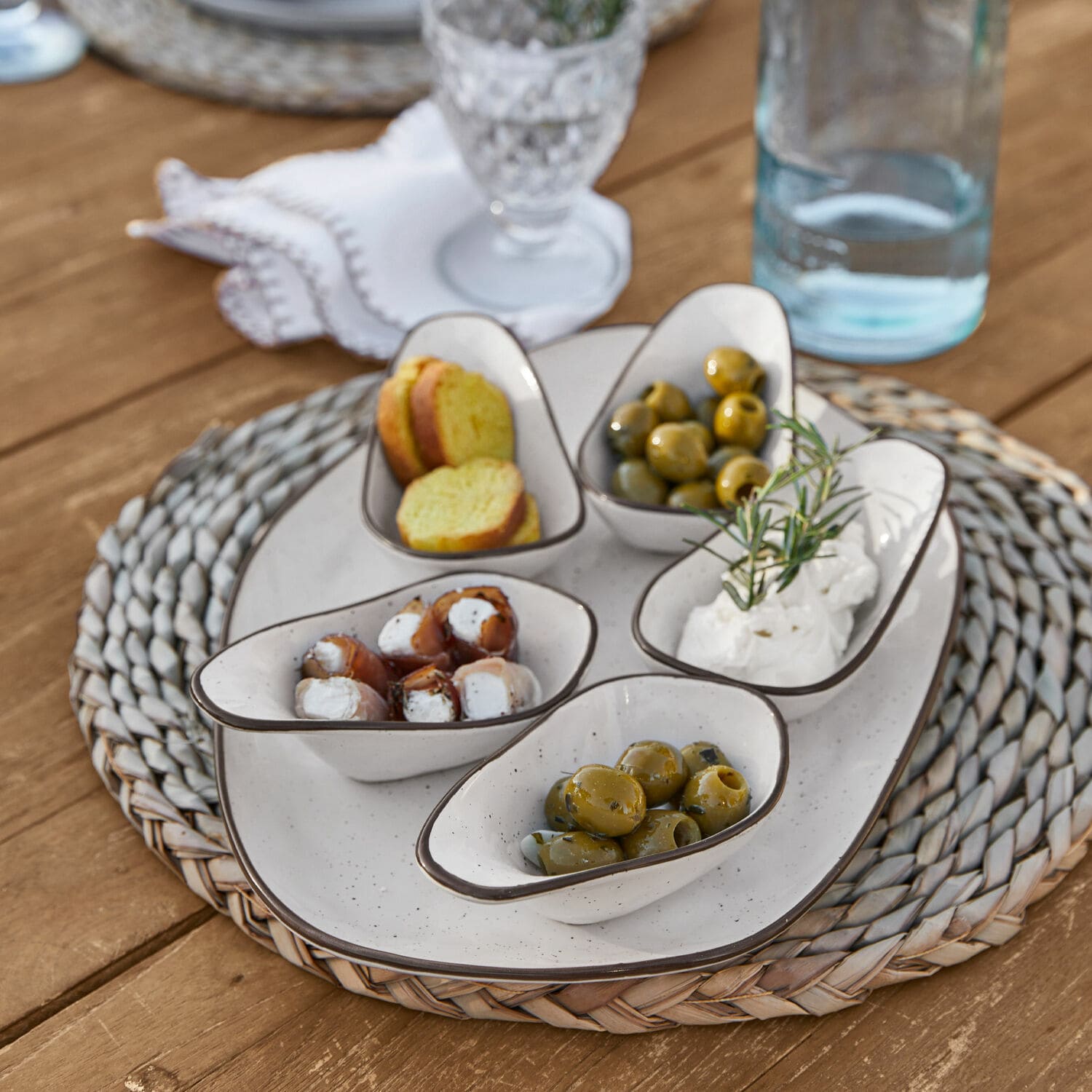 Serveerschaal set van 6 Biarré Witte keramische schaaltjes met olijven en kaas op gevlochten onderzetter op houten tafel