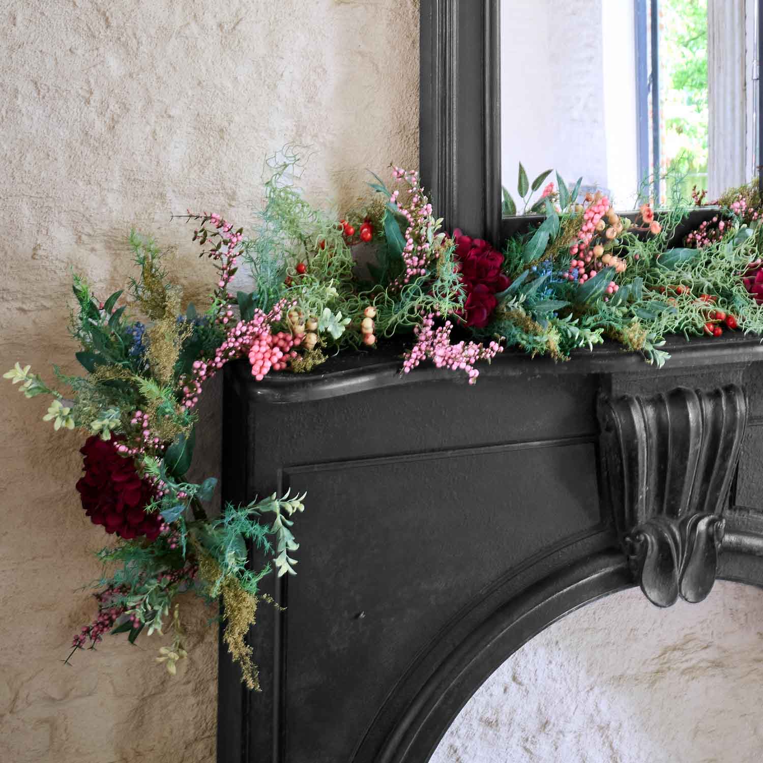 Guirlande décorative avec baies rouges et roses et feuillage vert sur une cheminée noire