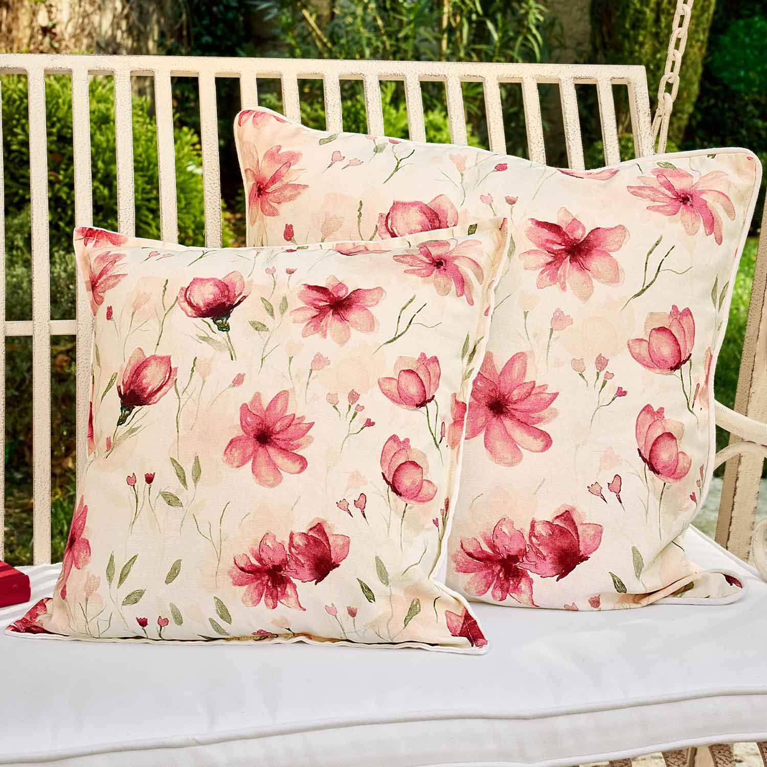 Deux coussins carrés en coton crème avec motif floral rose, parfaits pour décorer un espace extérieur