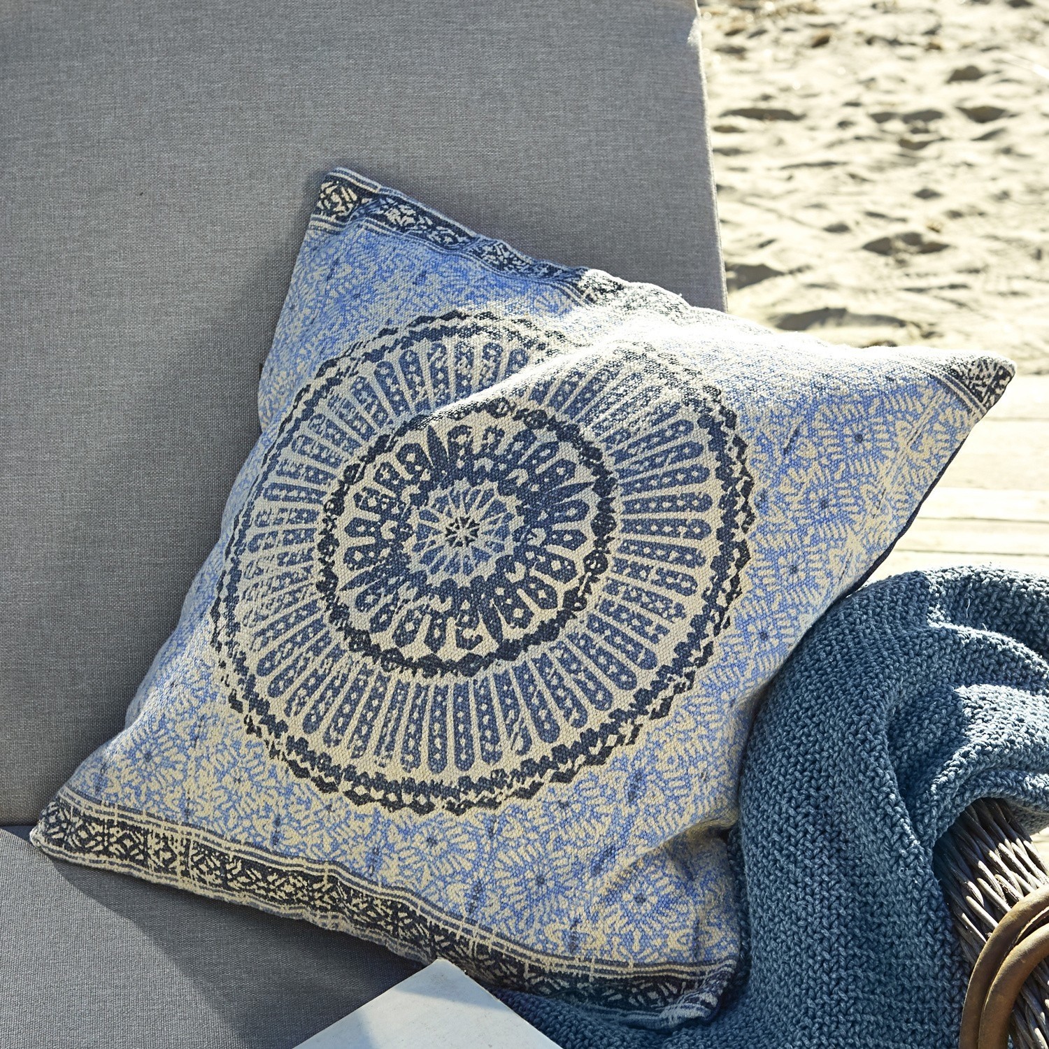 Coussin décoratif en coton bleu et beige avec motif oriental posé sur un canapé gris