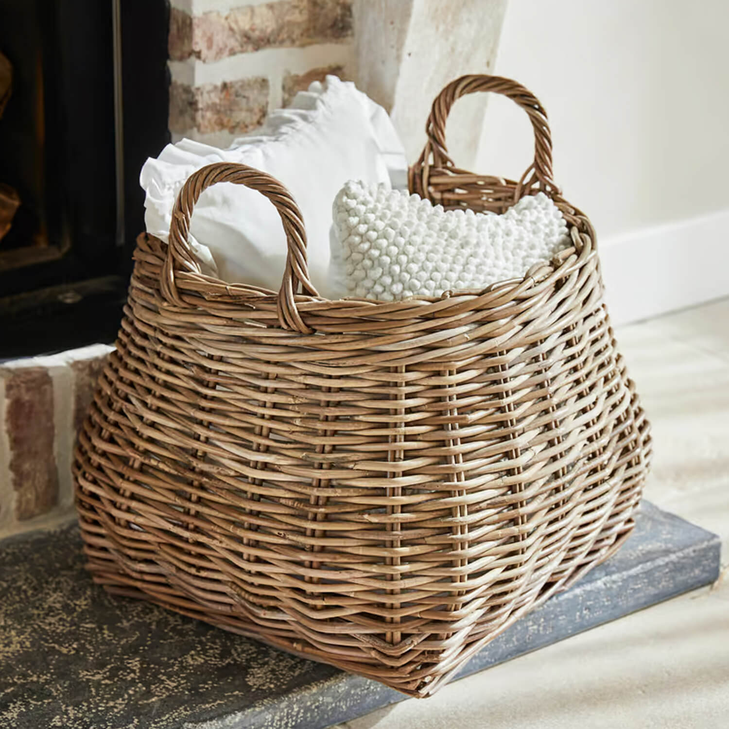 Panier en osier naturel avec poignées, rempli de coussins blancs, idéal pour rangement et décoration intérieure