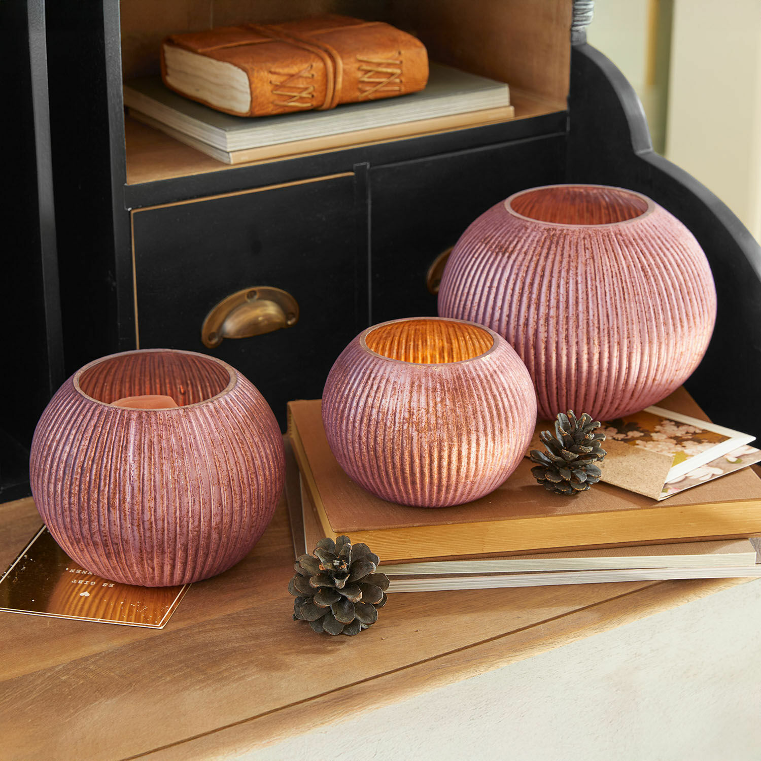 Lot de 3 photophores Jalimeen Ensemble de trois photophores en verre rose côtelé posés sur une table en bois avec décorations naturelles