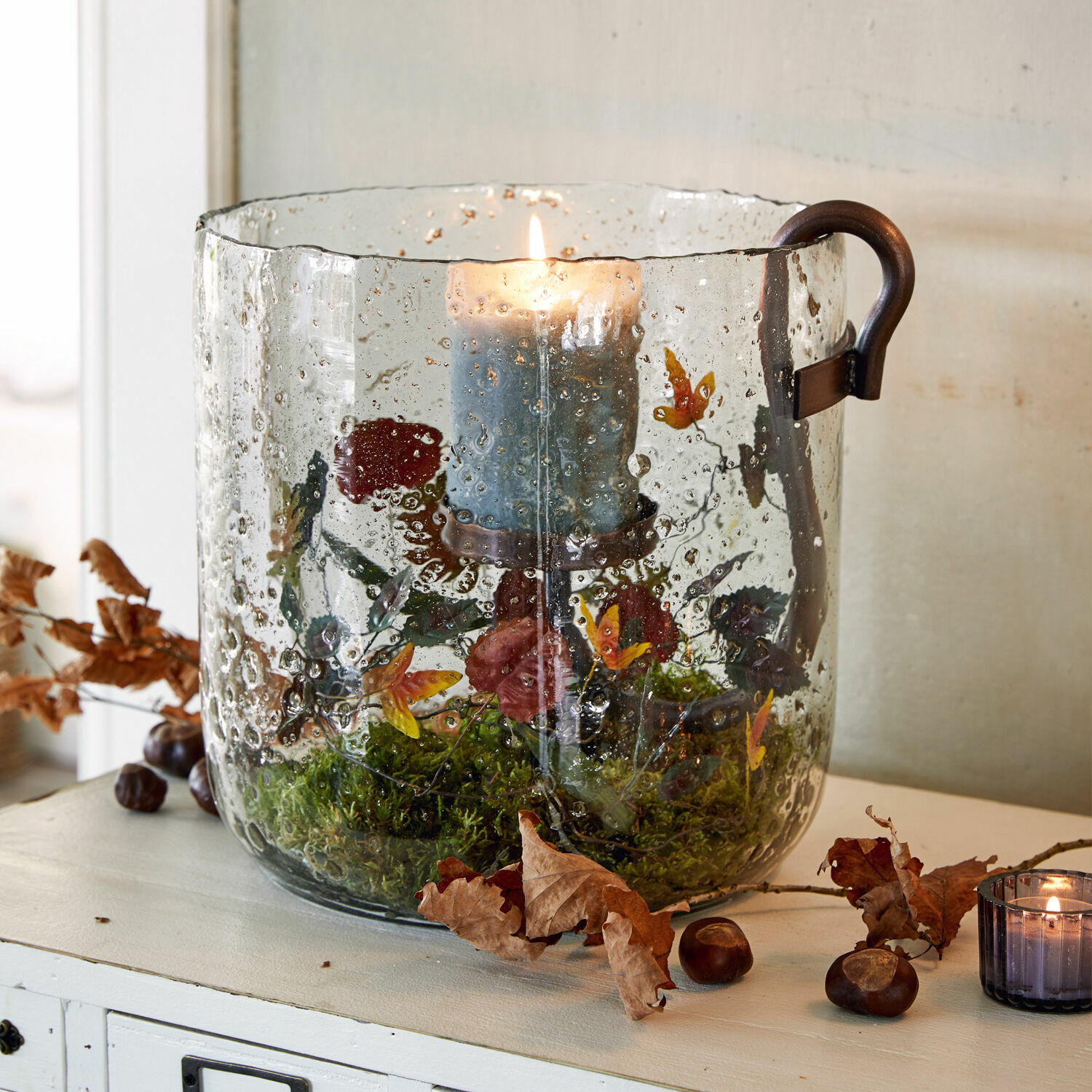 Windlicht Dions Glazen windlicht met handvat en blauwe kaars, versierd met mos en bloemen, herfstdecoratie